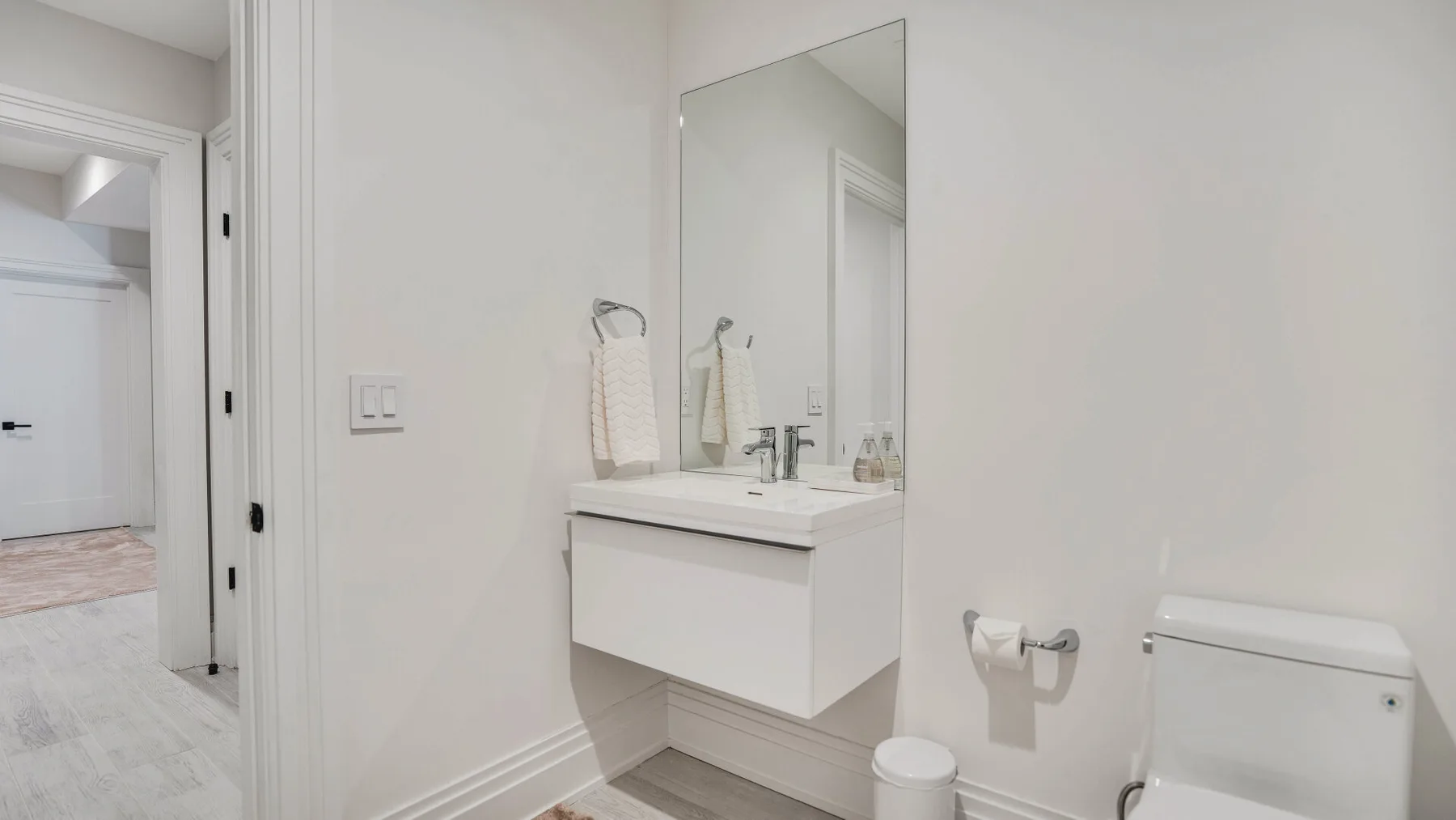 Un baño luminoso con lavabo suspendido, espejo e inodoro.