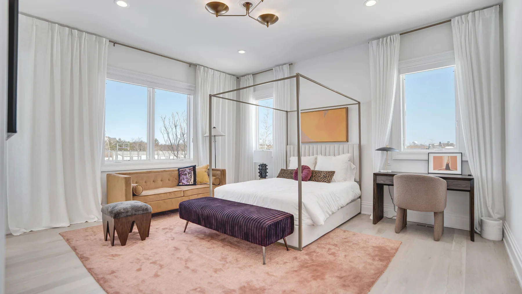 Un dormitorio luminoso con cama con dosel, escritorio y ventanas altas con cortinas.