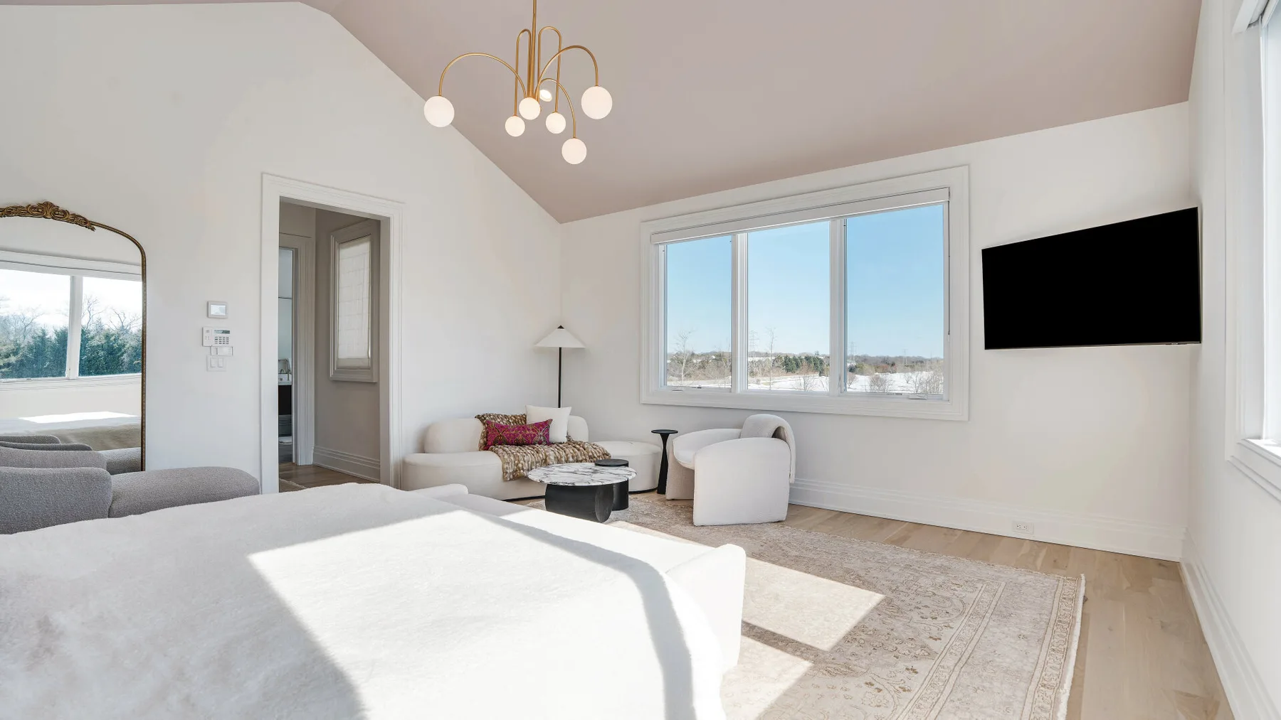 Un dormitorio luminoso con una cama, una zona de asientos y ventanas grandes.