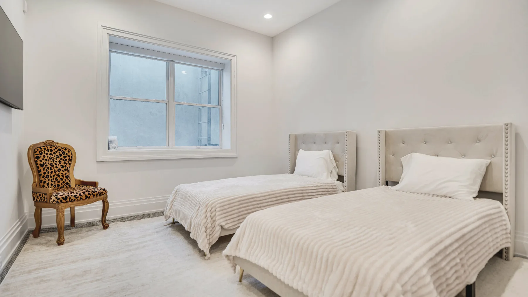 Un dormitorio luminoso con dos camas, una ventana y una silla estampada.