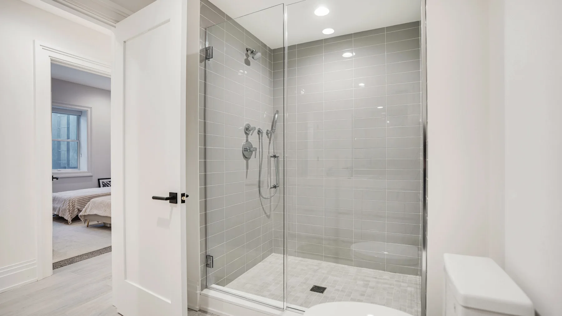 Una ducha con azulejos y mampara de vidrio está junto a una puerta abierta.