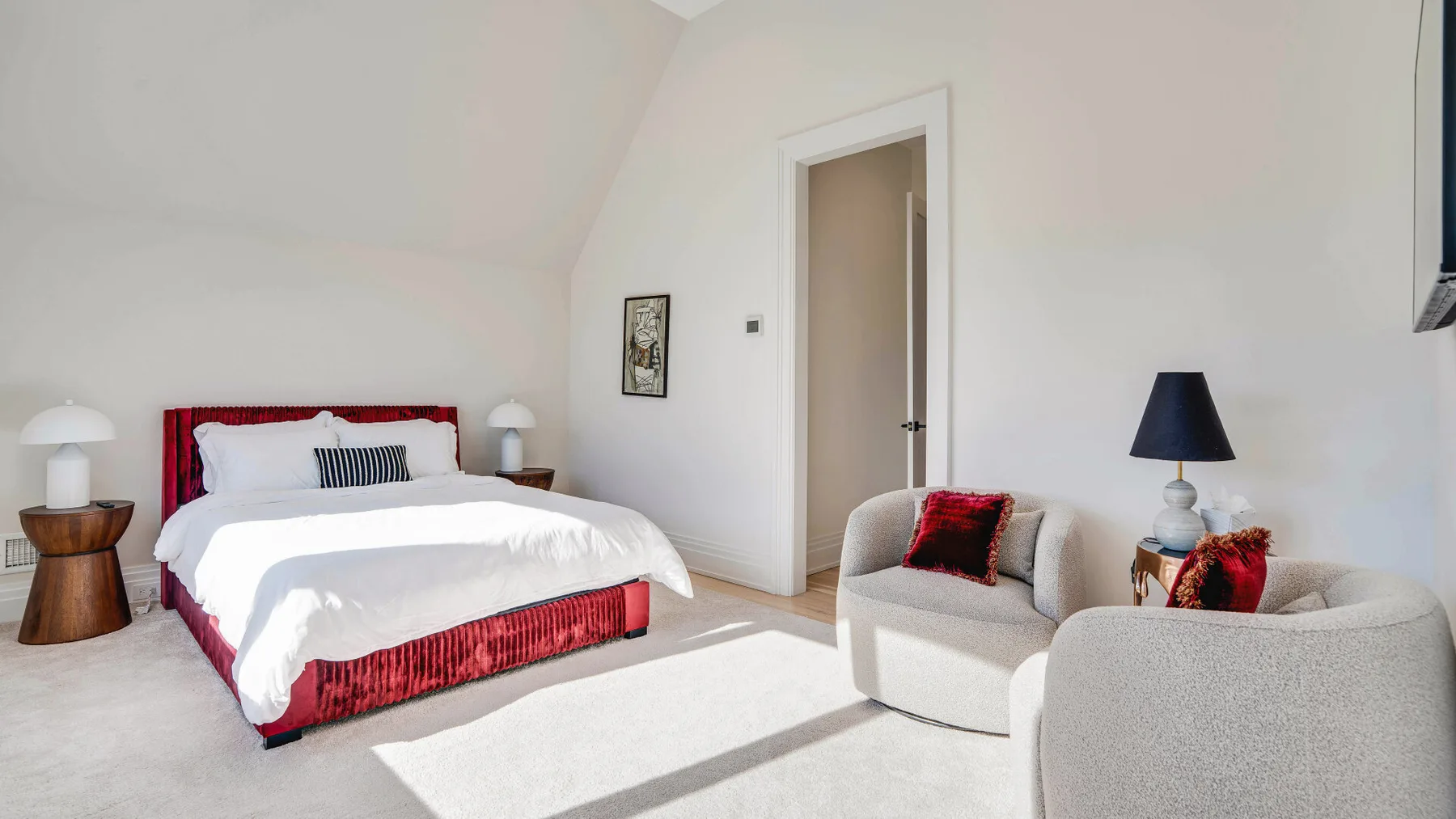 Un dormitorio luminoso con una cama roja y una zona de asientos junto a la puerta.