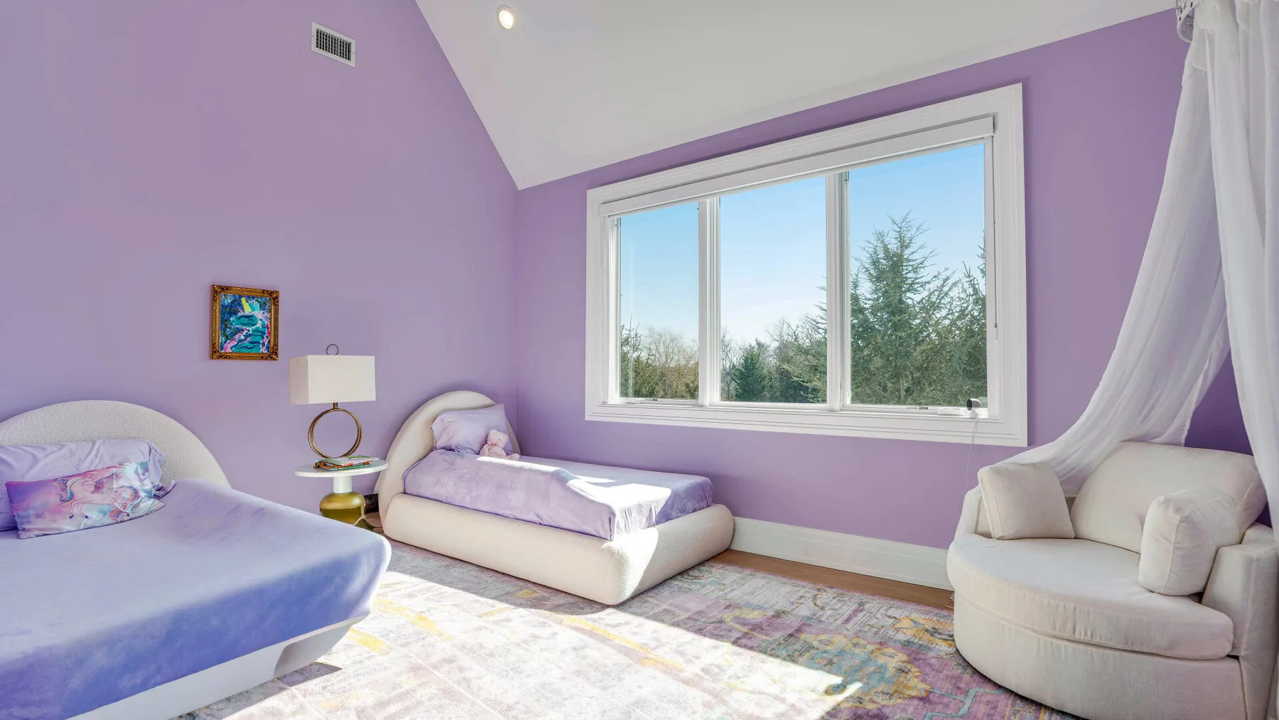 Un dormitorio lavanda con camas, un sillón acolchado y una ventana grande.