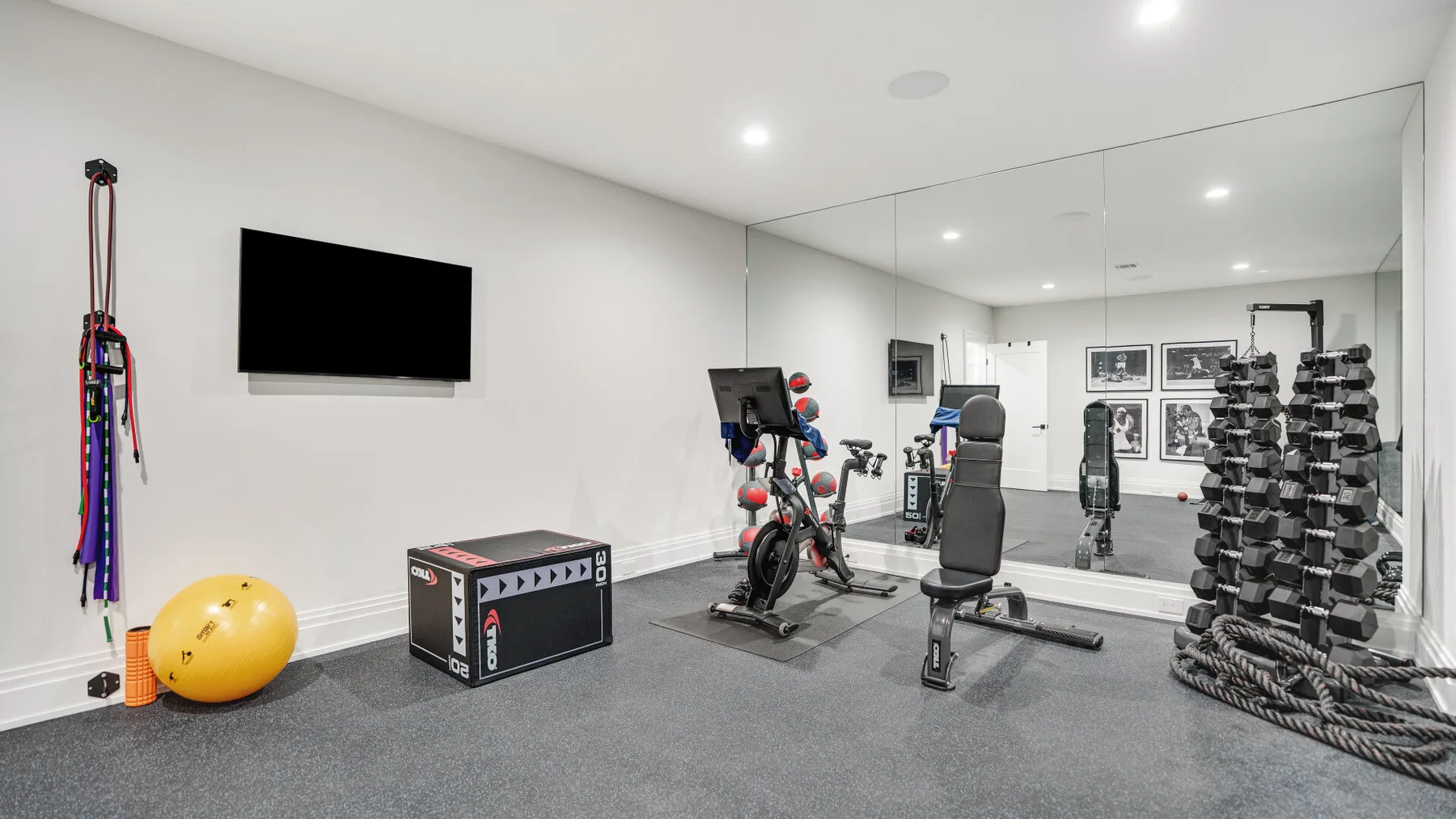 Un gimnasio en casa con equipo de ejercicio, una pantalla en la pared y paredes con espejos.
