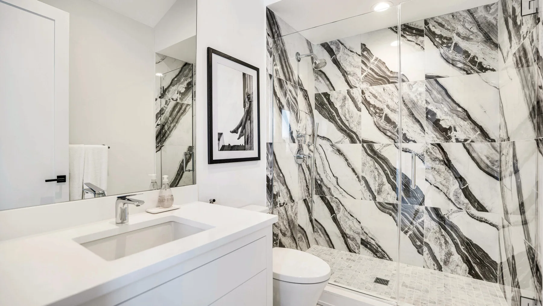 Un baño moderno con lavabo y una ducha con paredes de efecto mármol.
