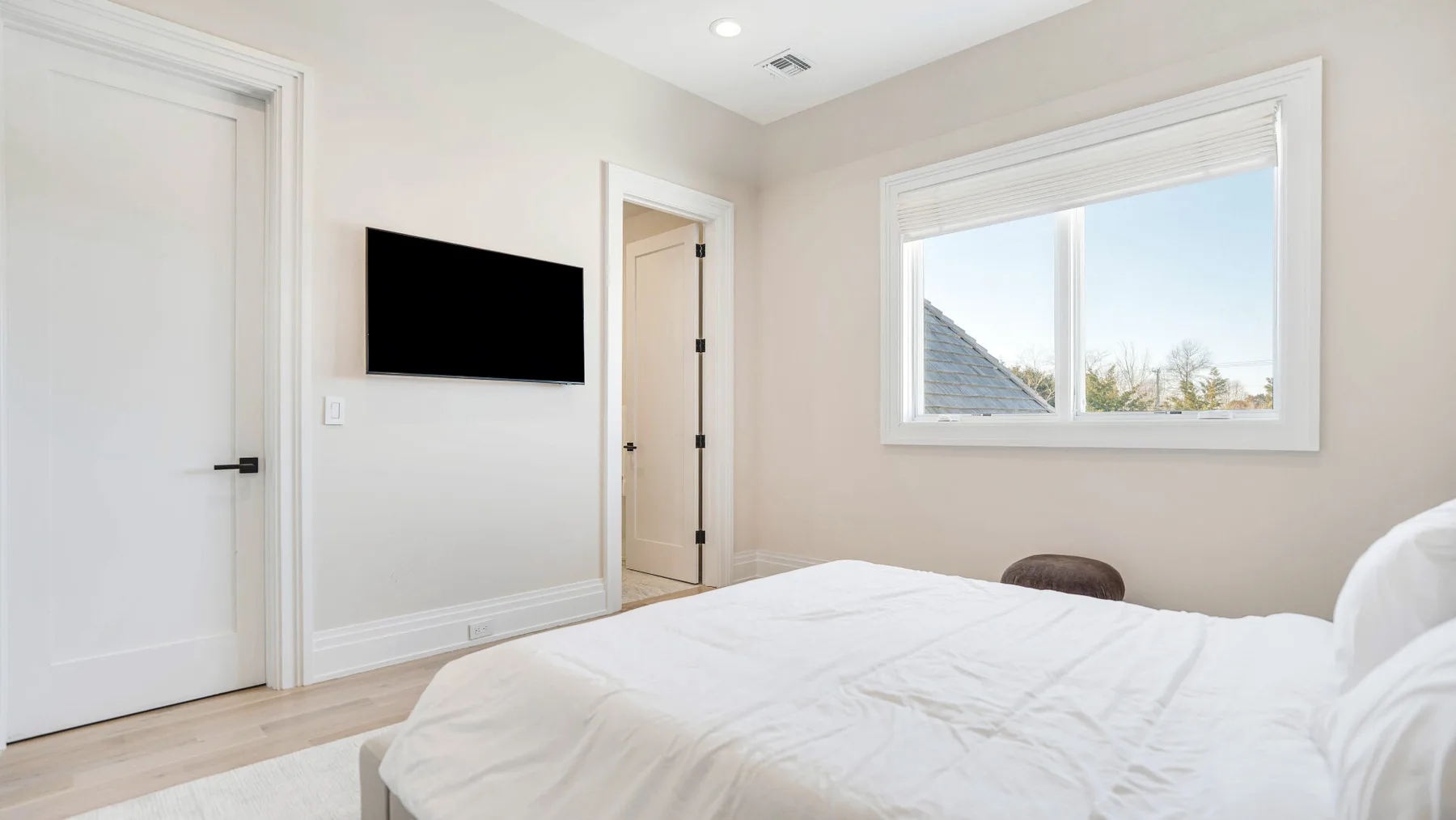 Dormitorio con una cama bien tendida, un televisor en la pared y una ventana.