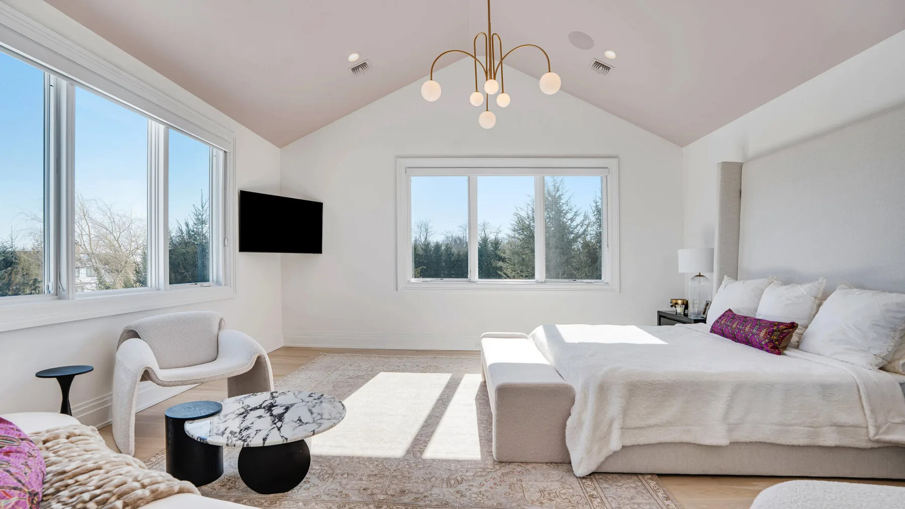 Un dormitorio luminoso con una cama grande, asientos y amplias ventanas.