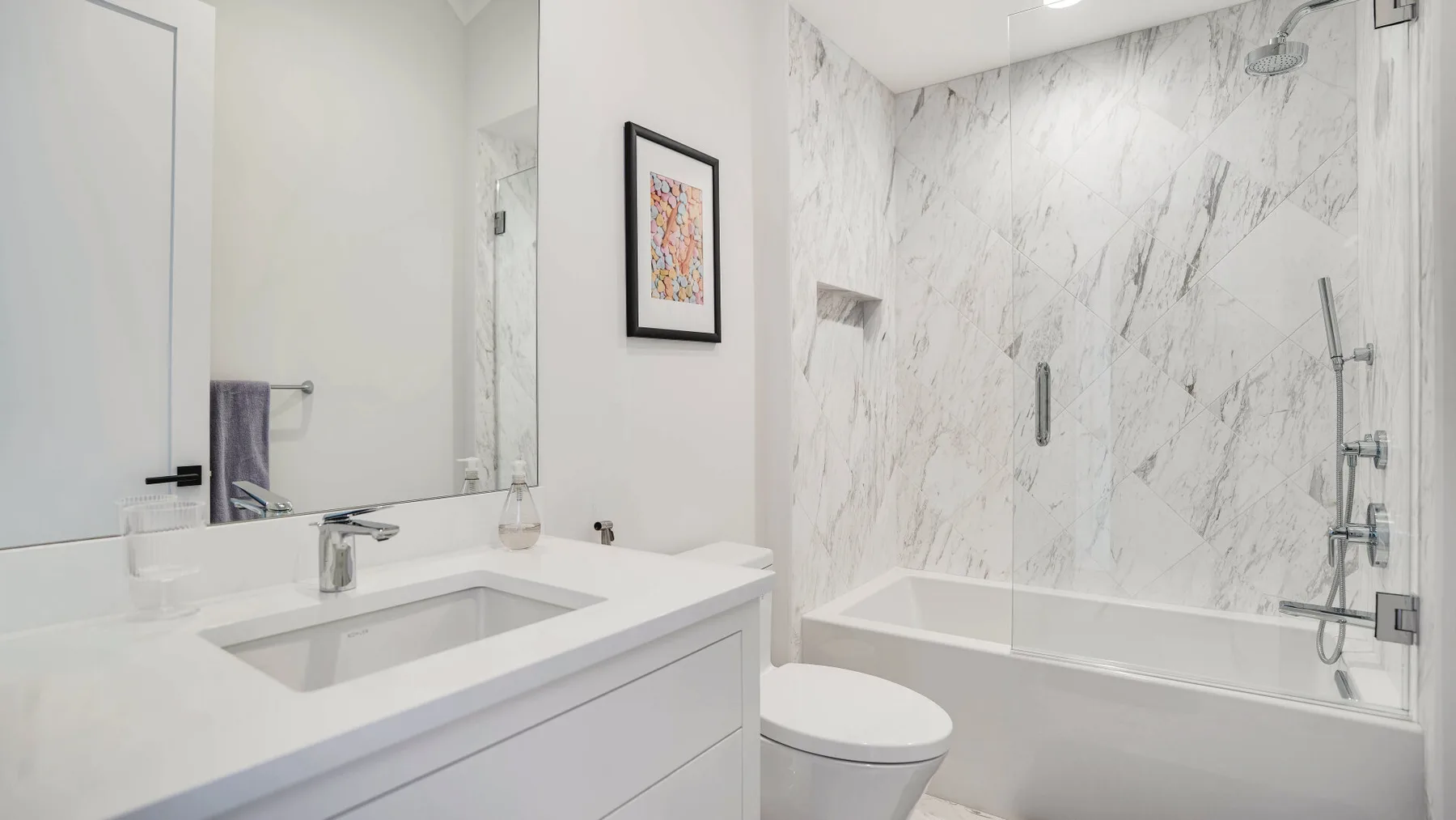 Un baño luminoso con un tocador blanco y una zona de ducha y bañera con acabado tipo mármol.