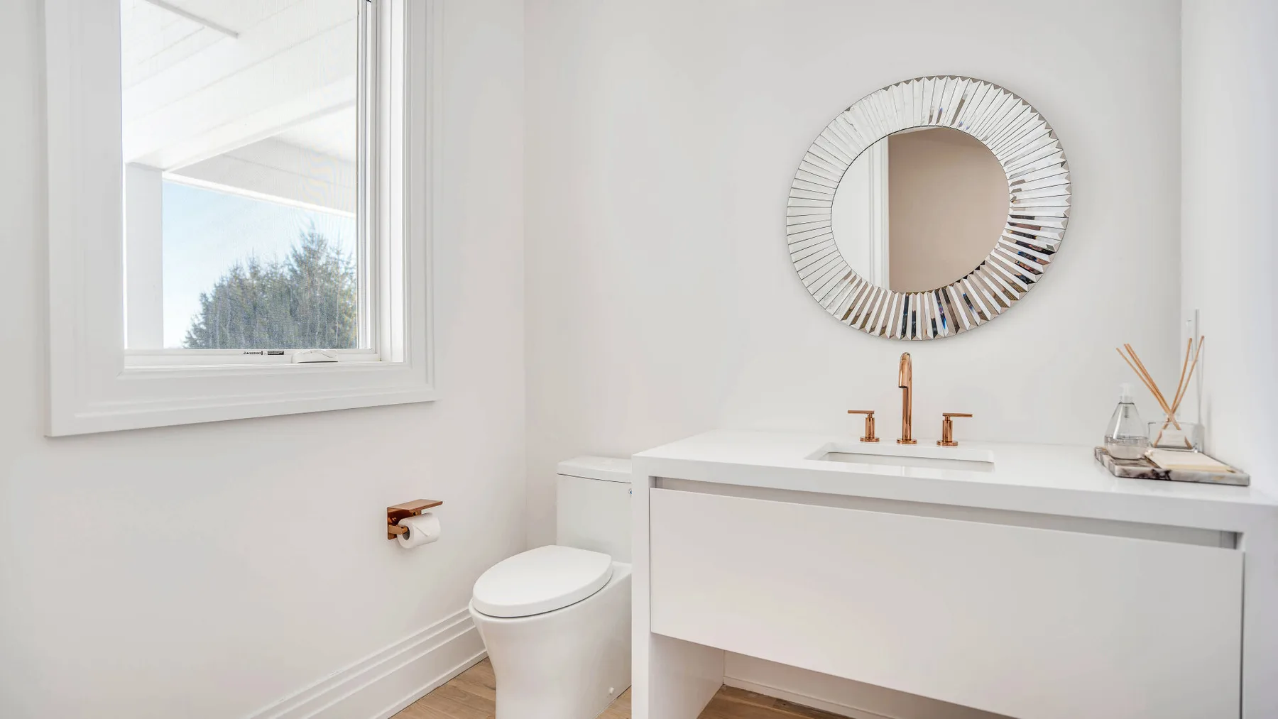 Un baño luminoso con un mueble de lavabo blanco, inodoro y espejo redondo.