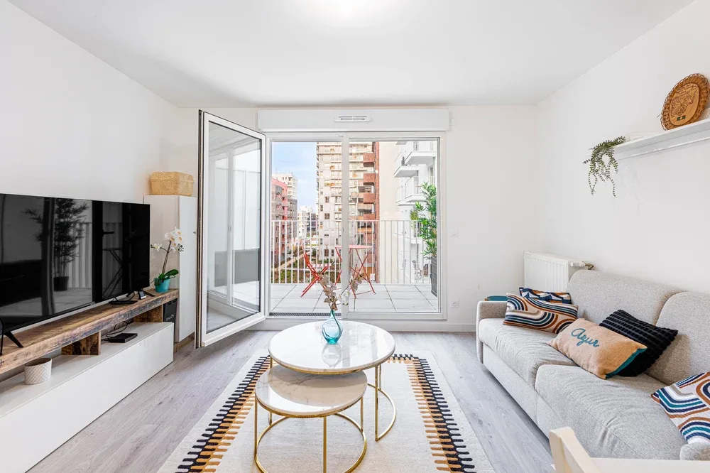 A bright living room with seating, a television, and an open balcony door.