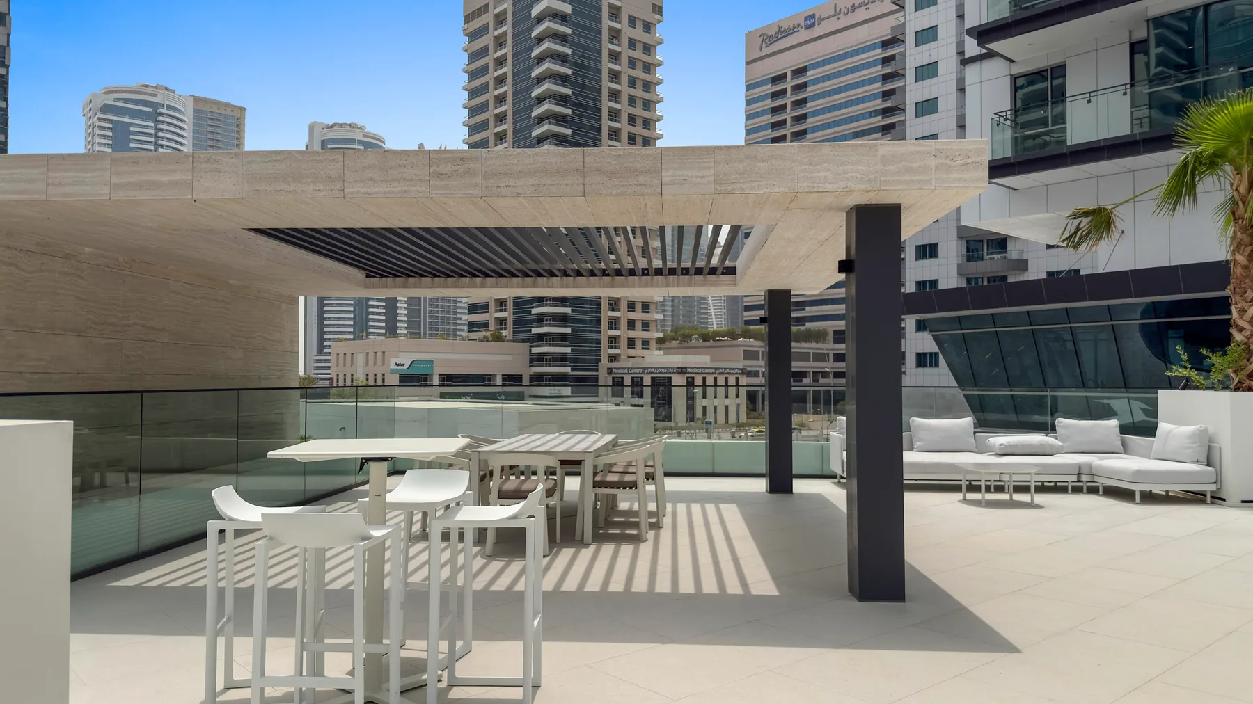 A rooftop terrace has white seating and a shaded dining area.