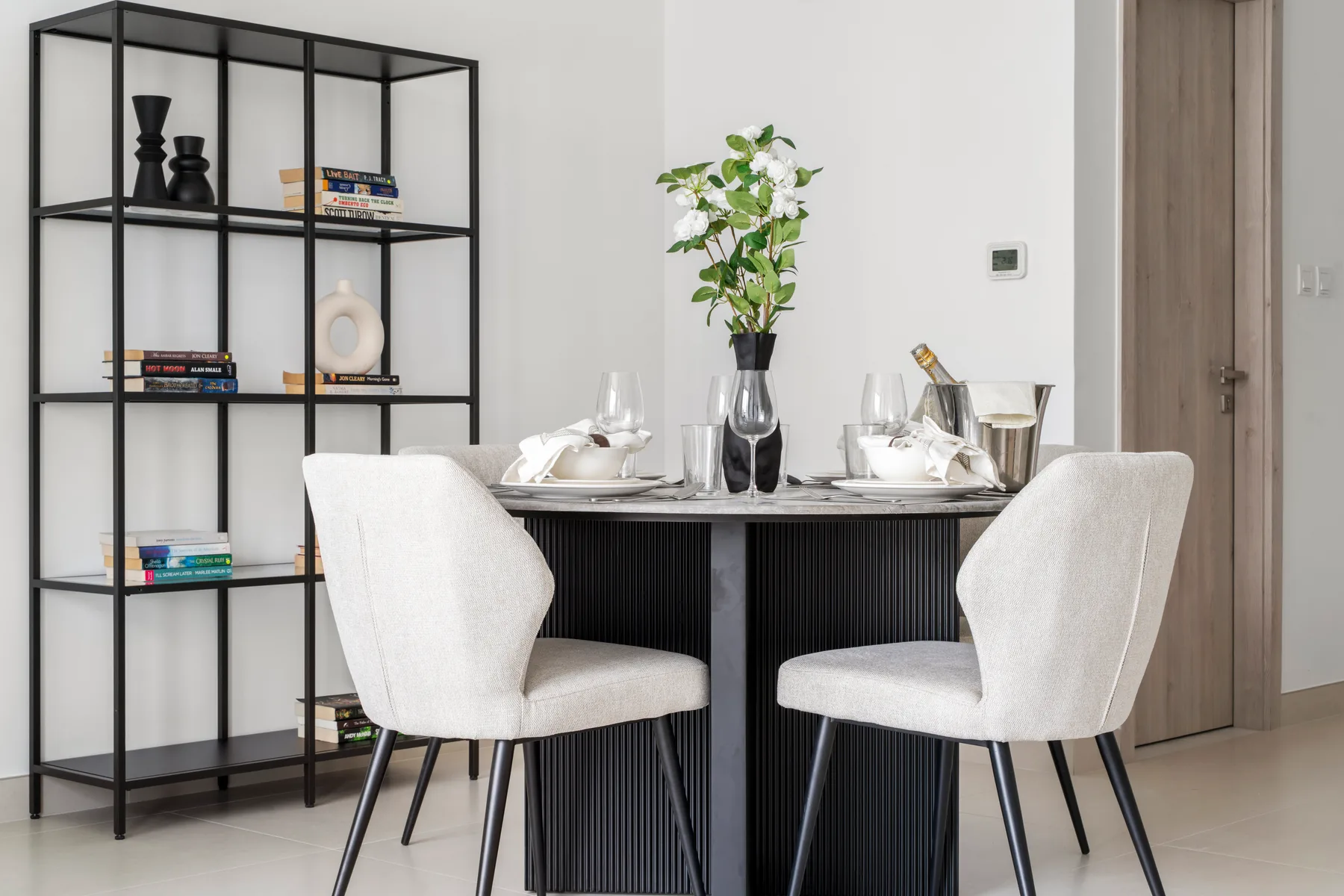 A dining area with a set table, upholstered seating, and an open shelving unit.