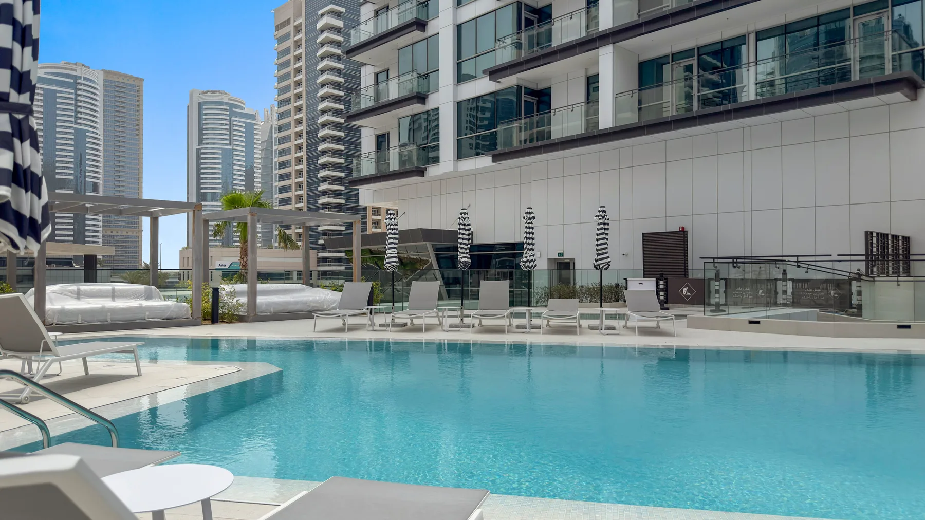 A rooftop pool beside a modern high-rise building, with lounge seating around the water.
