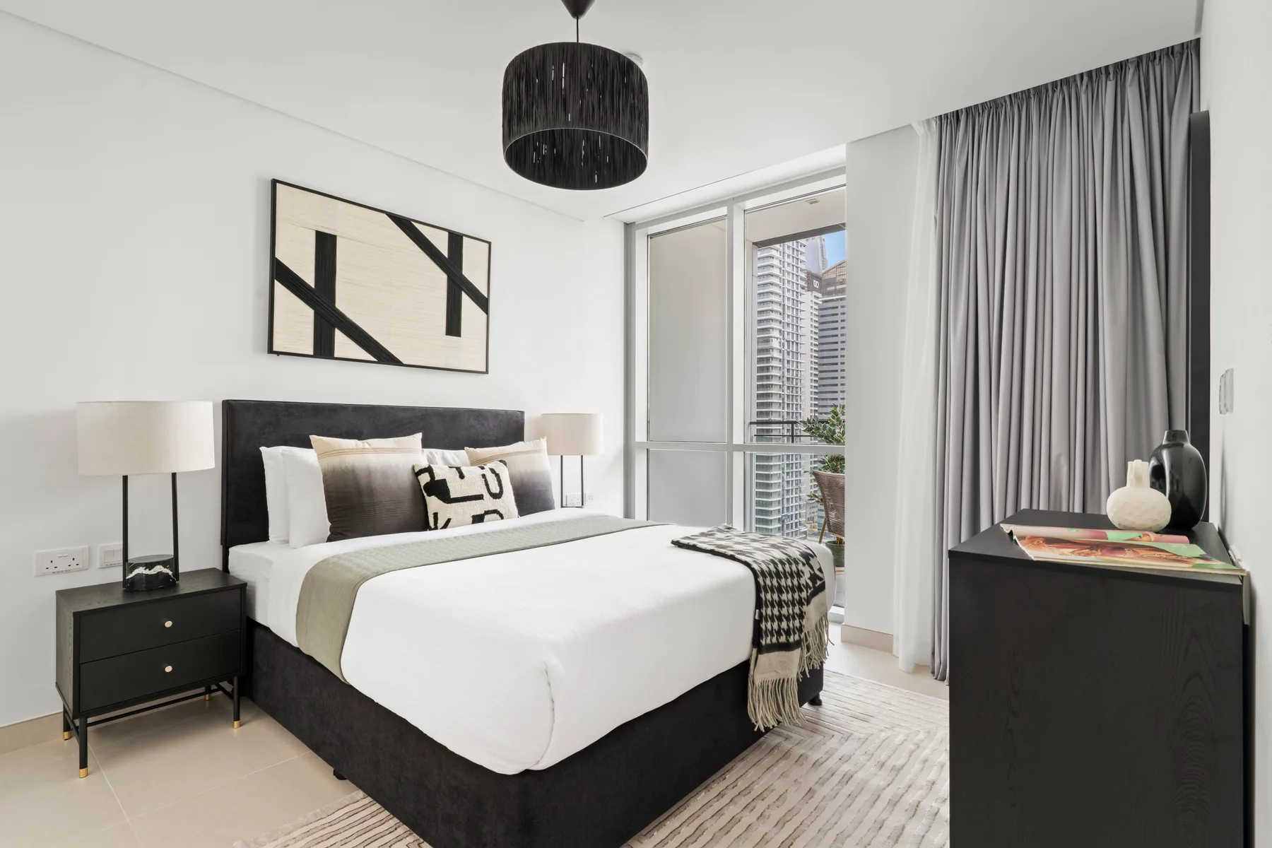 A bright bedroom with a large bed beside a window and floor-length curtains.