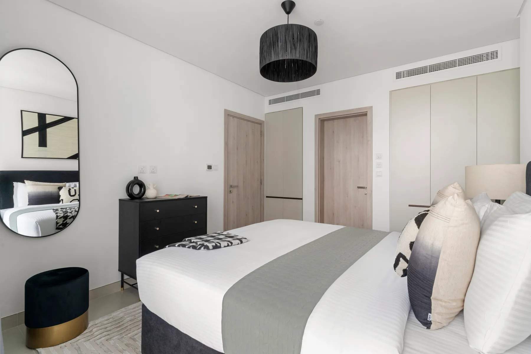 A bright bedroom with a neatly made bed and a dark pendant light.