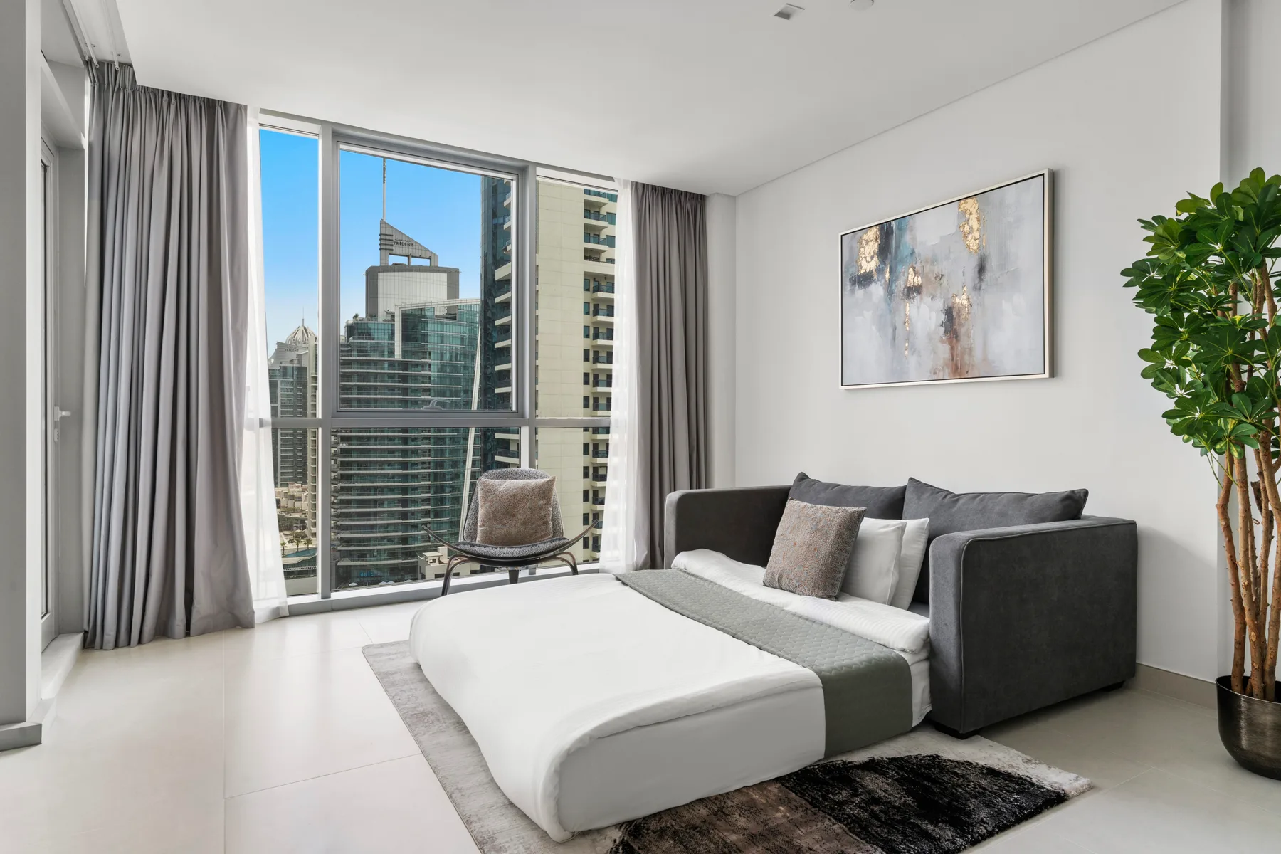 A bright living room has floor-to-ceiling windows, a sofa, and a low table.