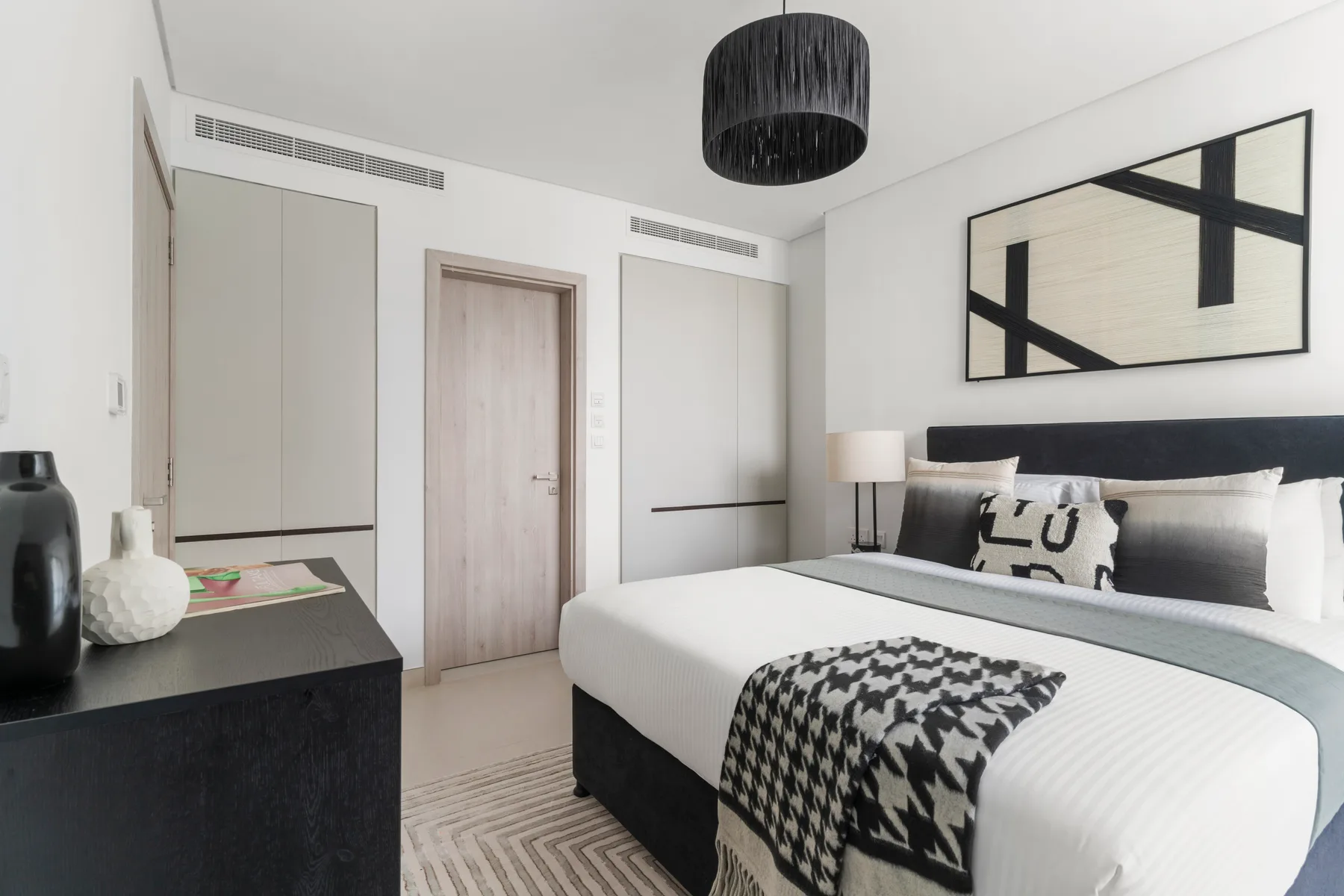 A modern bedroom with a neatly made bed and abstract artwork above the headboard.