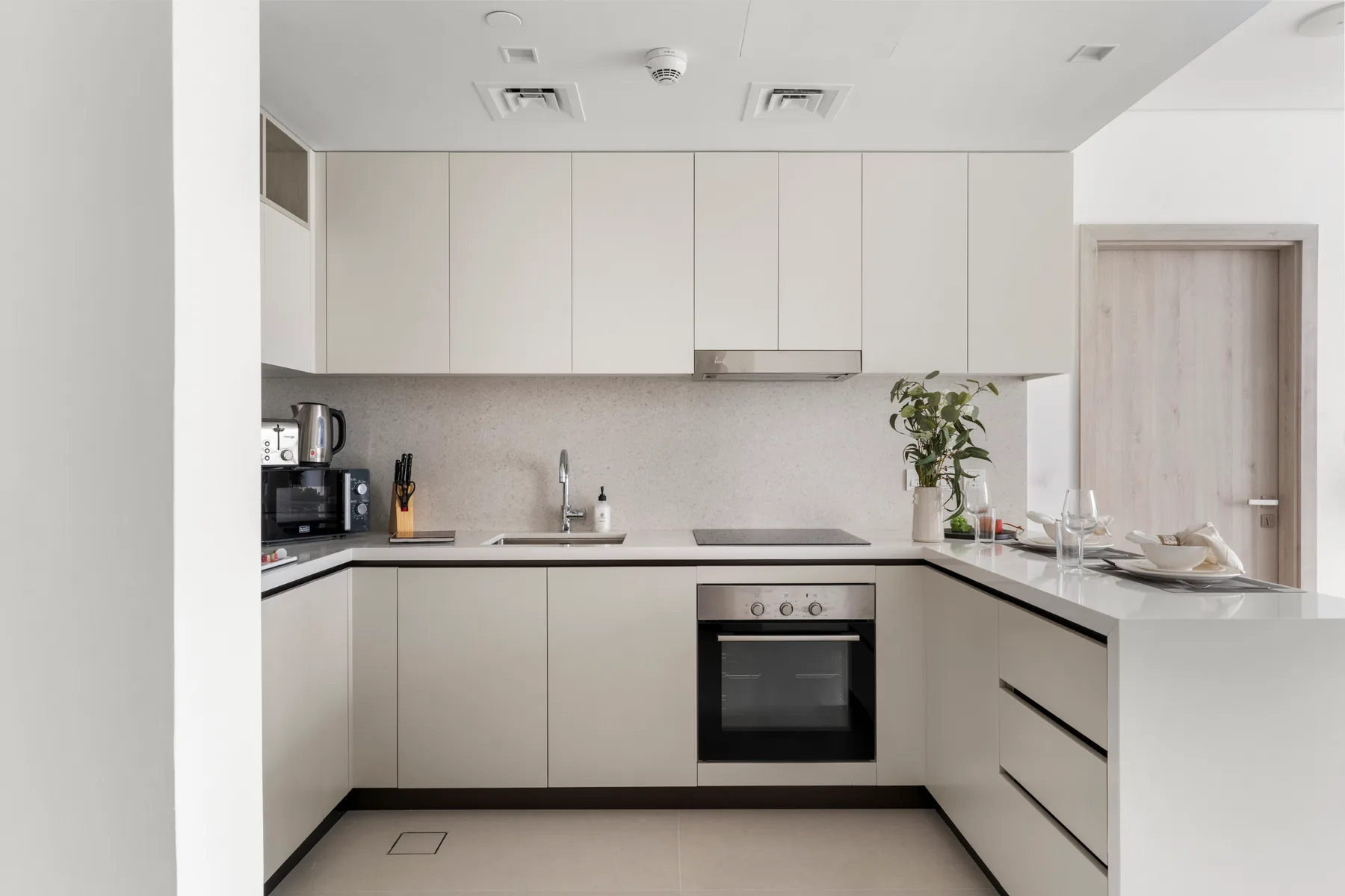 A modern kitchen with pale cabinetry, a dark cooktop, and a countertop plant.