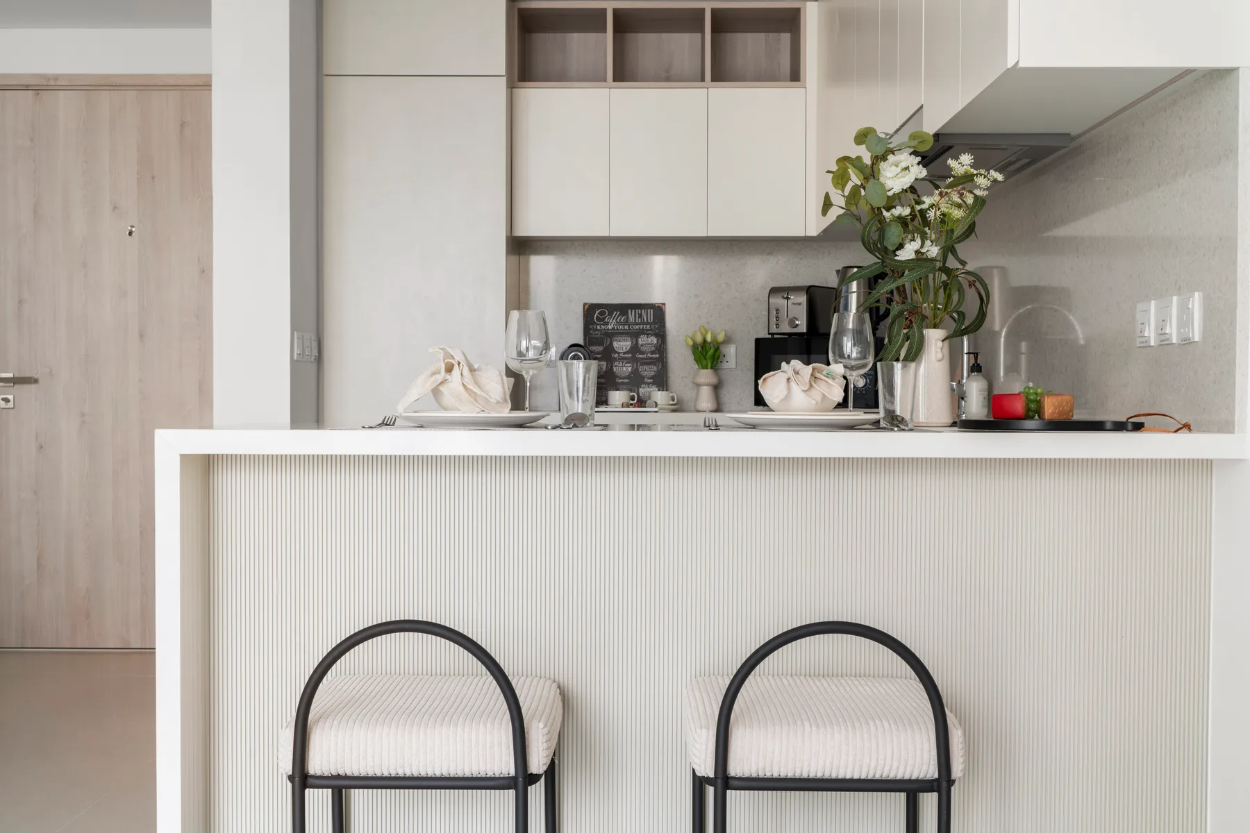A modern kitchen with a counter, two stools, and cabinets.