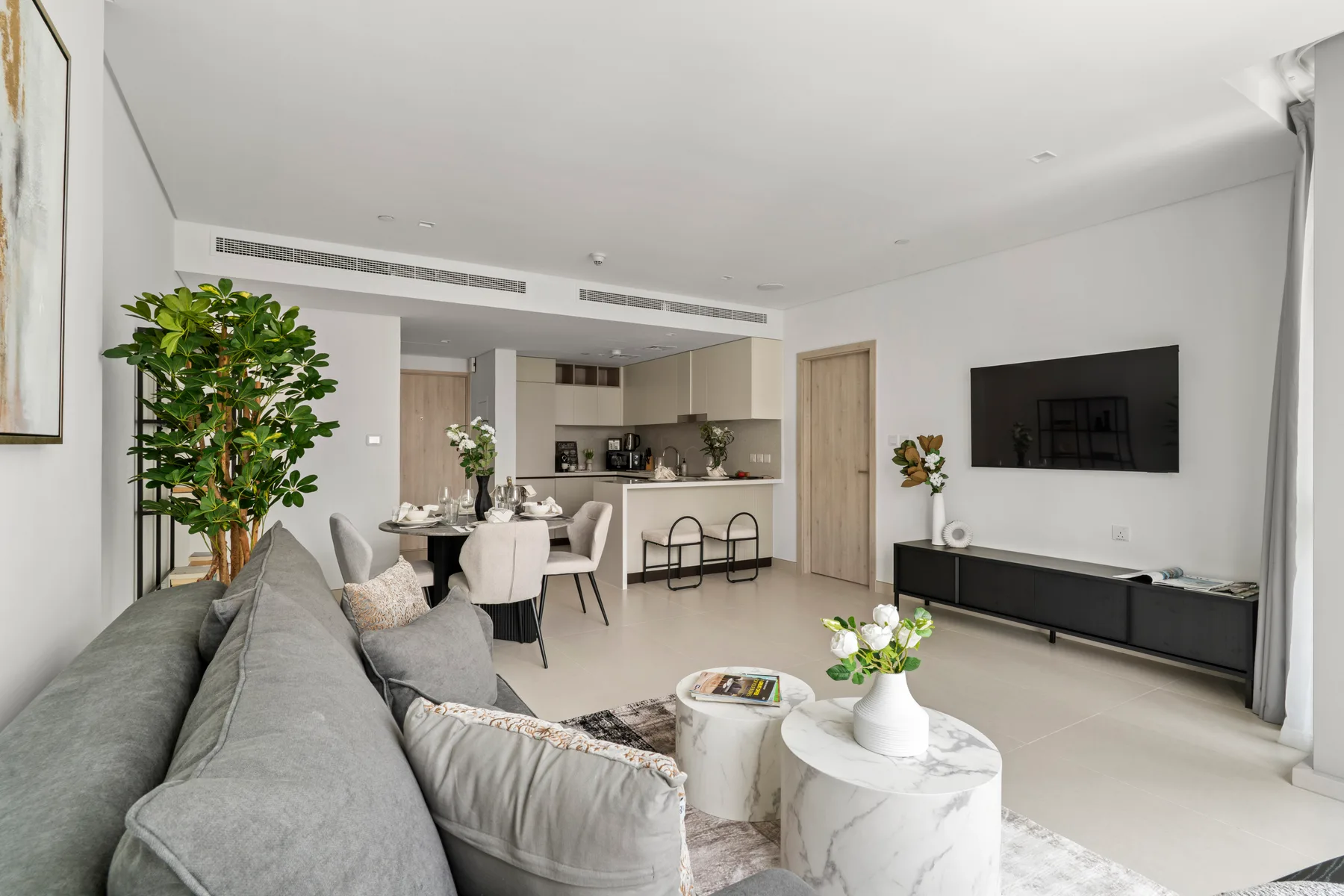 A bright living room with a seating area, coffee tables, and a wall-mounted television.