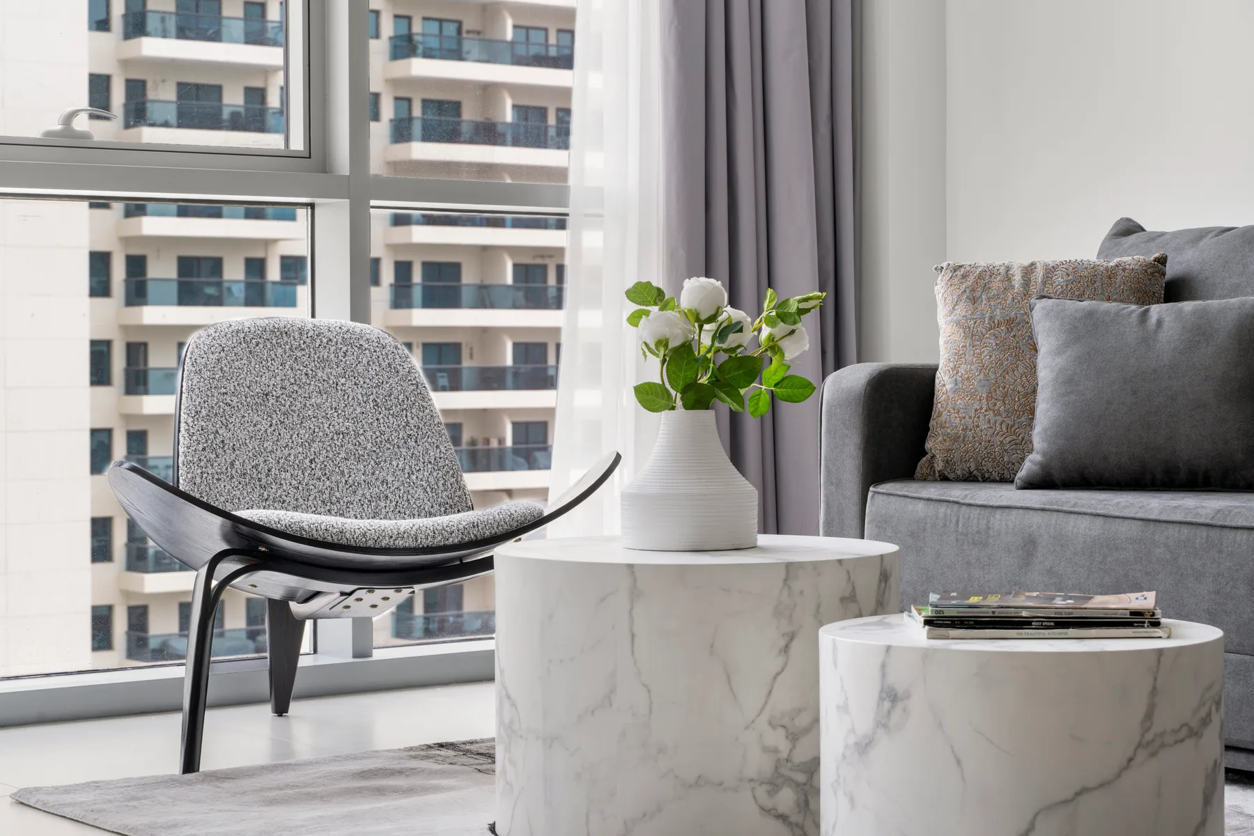 A bright living room with seating beside a large window and small tables.