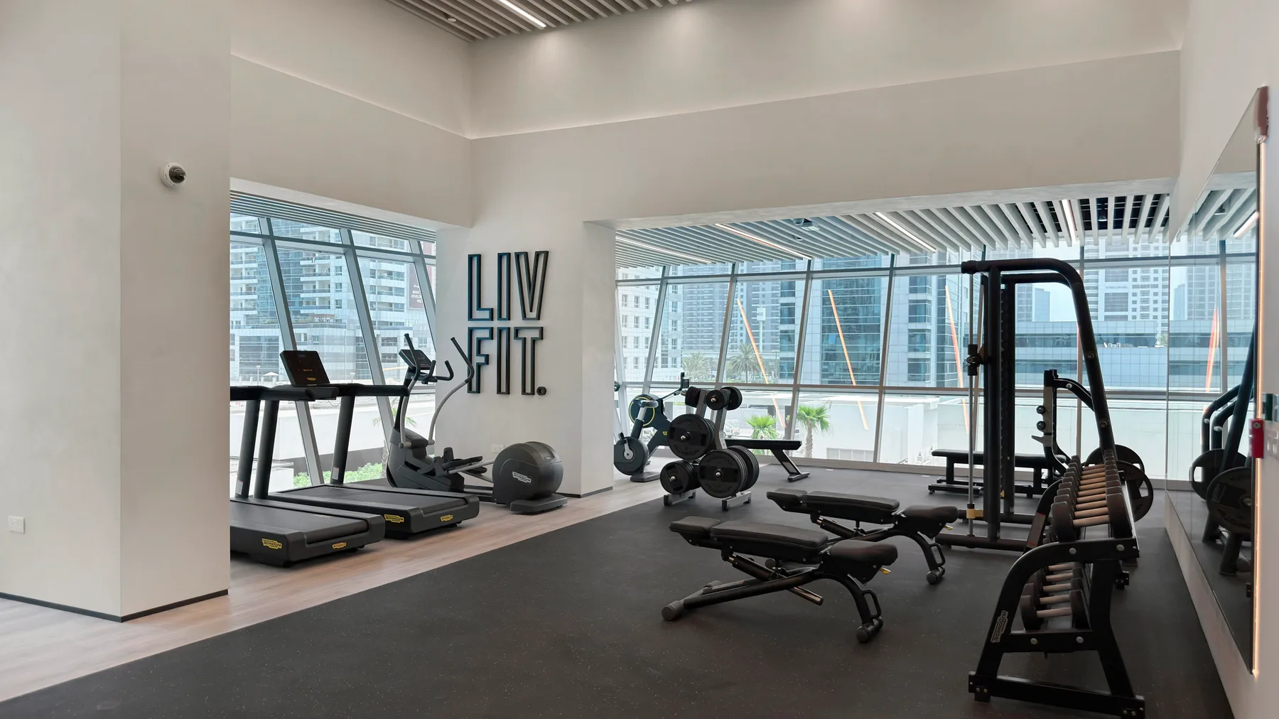 A bright gym with exercise machines, weights, and large windows.