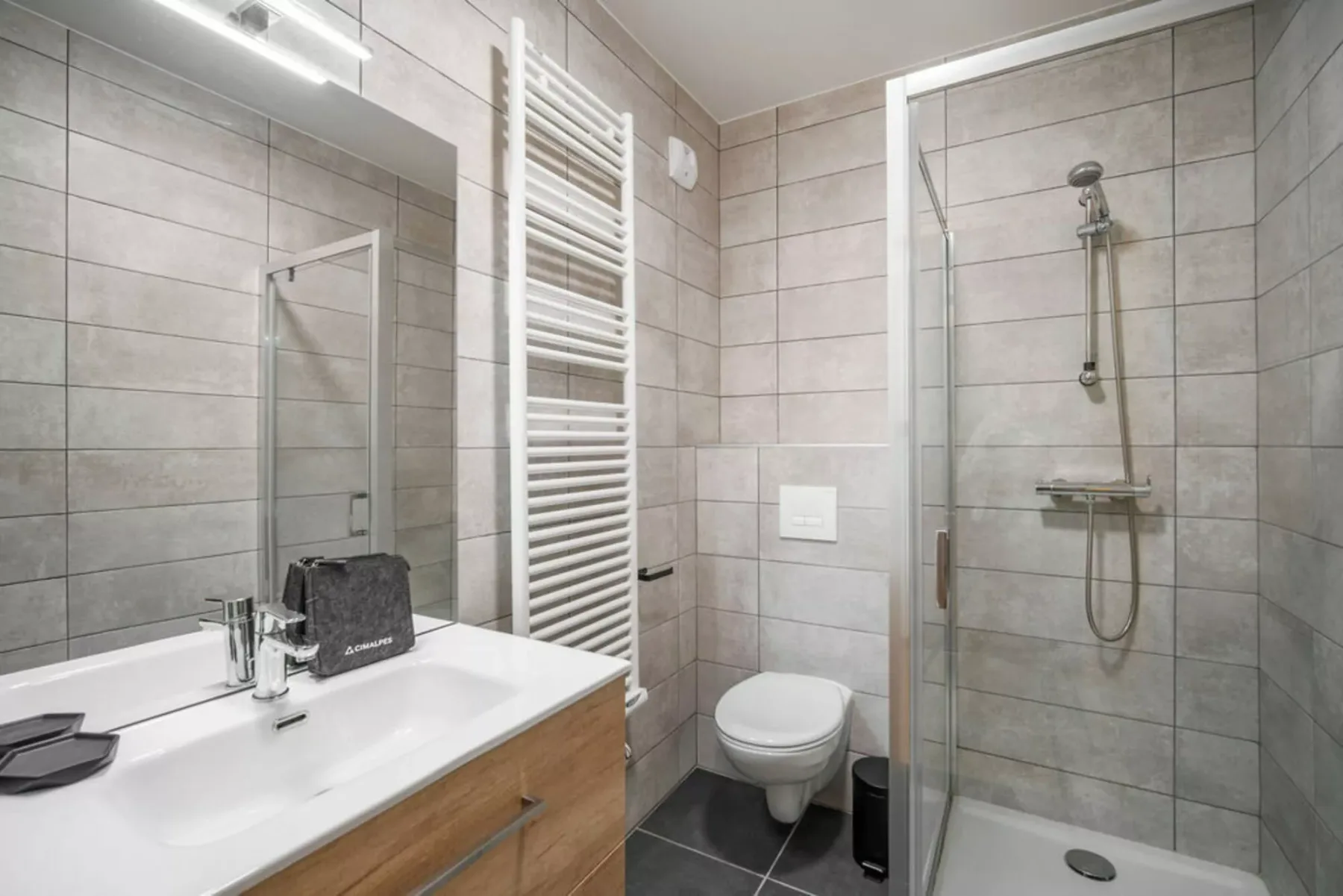 A tiled bathroom with a sink, wall-mounted toilet, and glass shower.