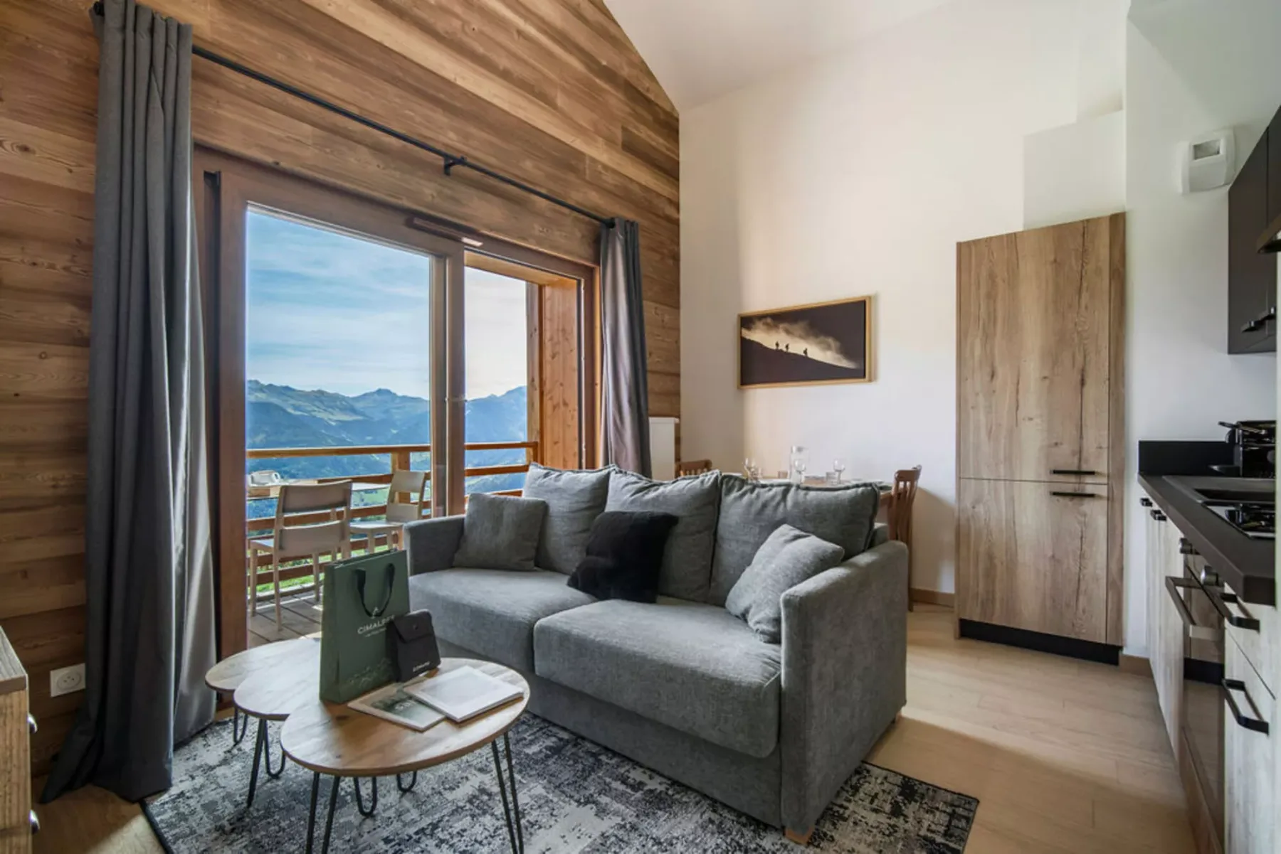 A living area with gray seating beside a large window overlooking mountains and water.