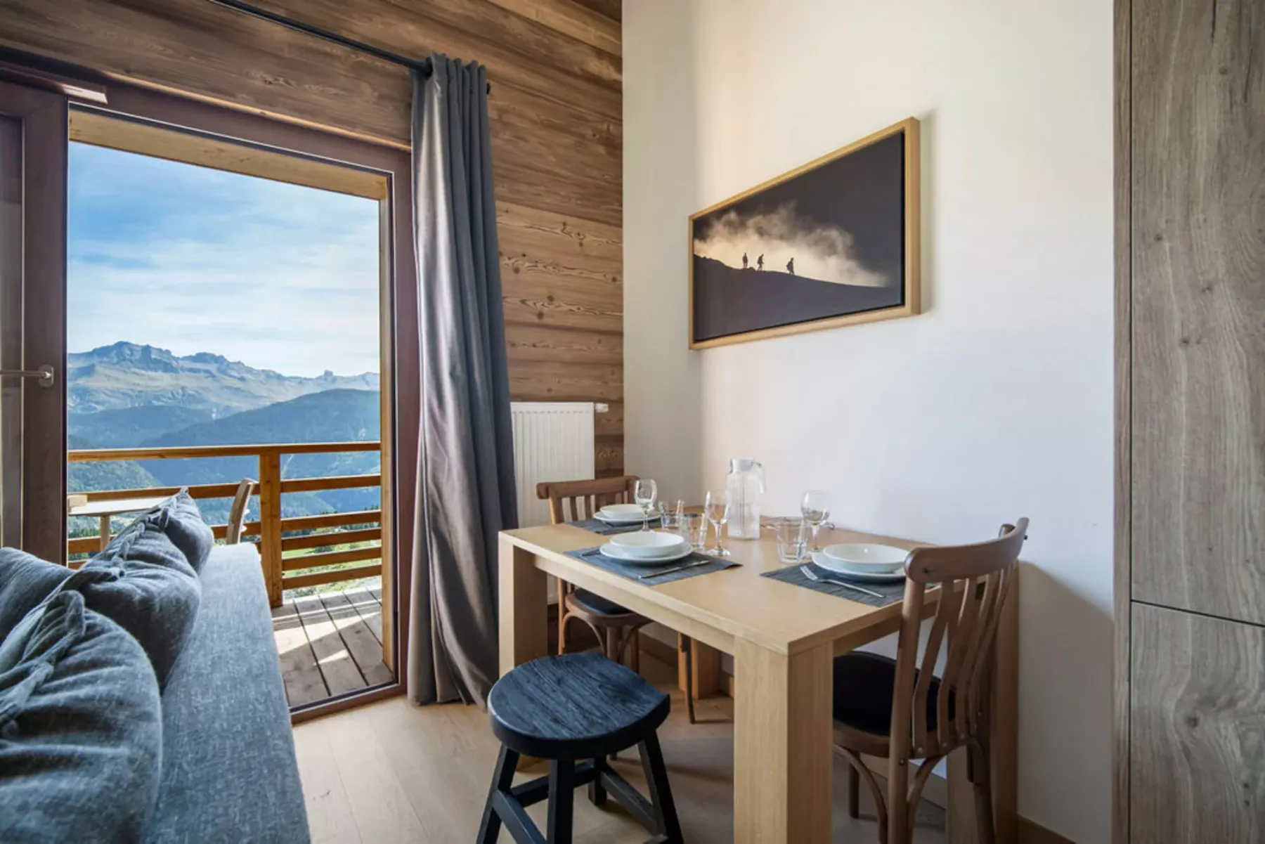 A dining area with a wooden table beside a glass door opening to a mountain view.