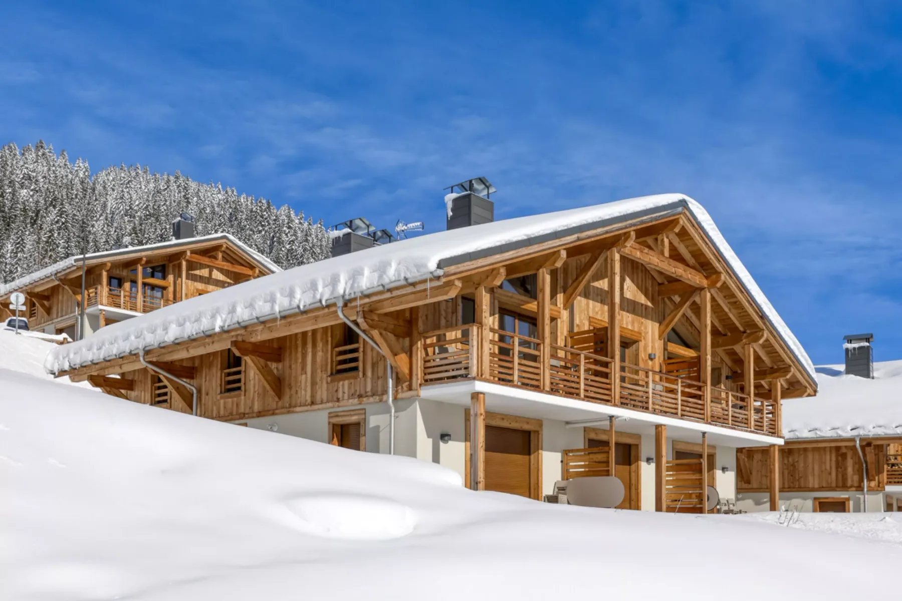 A wooden chalet stands in a snowy landscape beneath a clear blue sky.