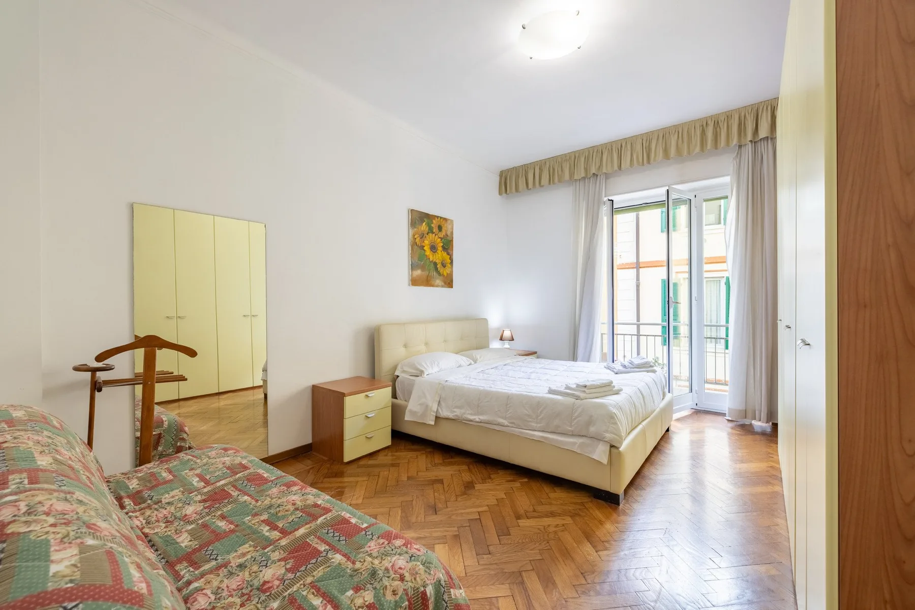 Un dormitorio con una cama, un sofá estampado y una puerta al balcón.