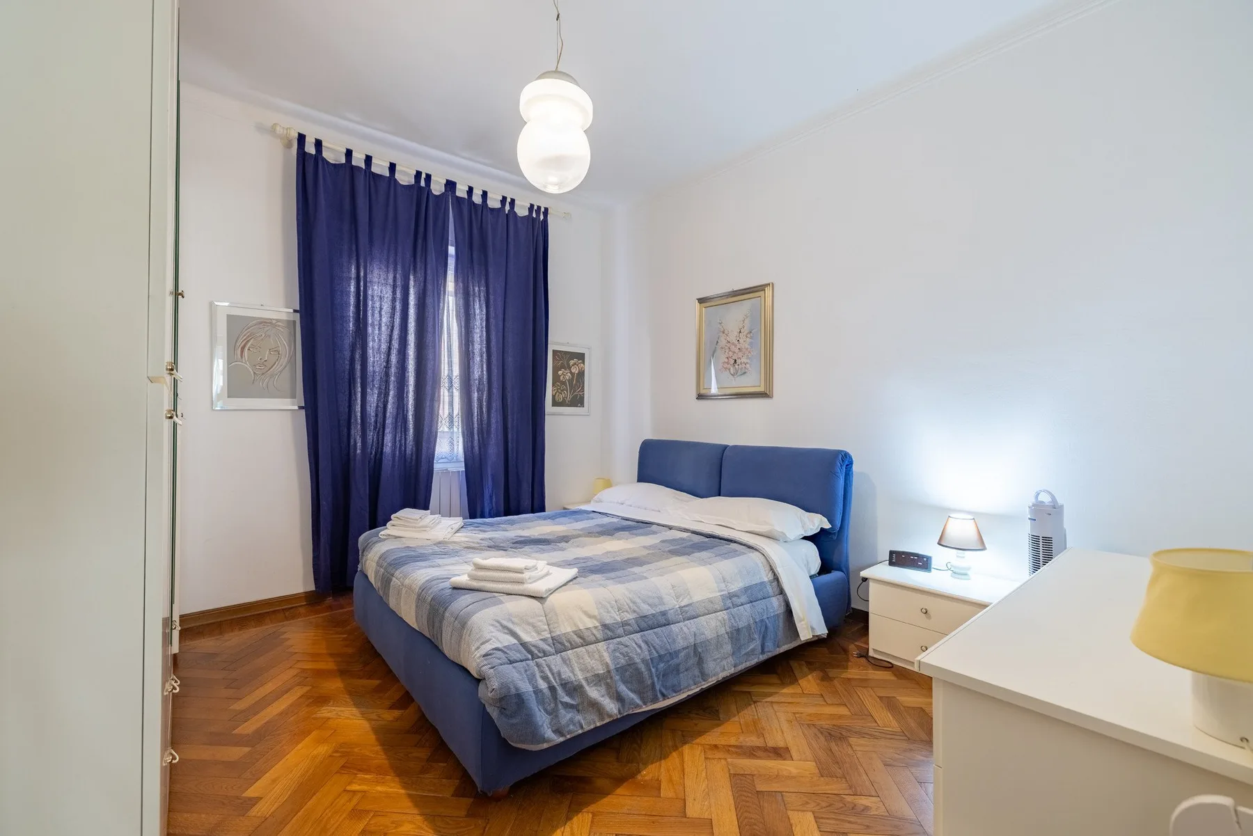 A bedroom with a blue bed, patterned bedding, and dark curtains.