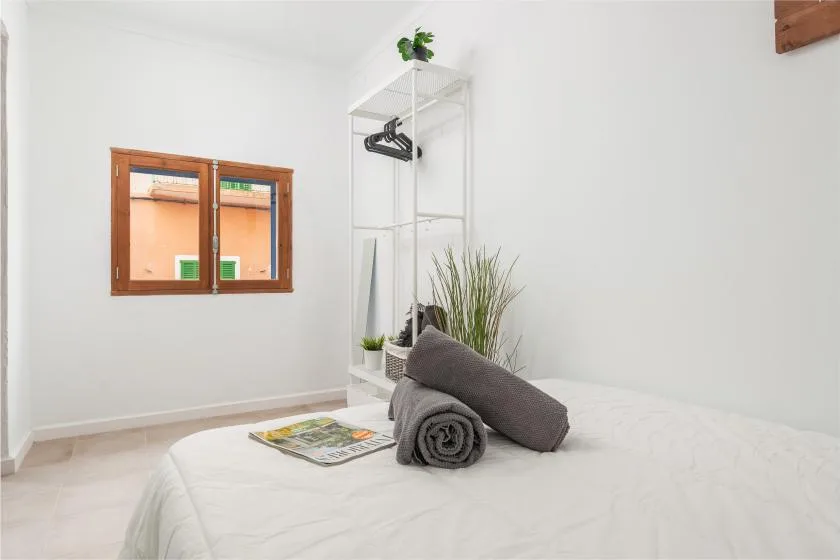 A bright bedroom with a neatly made bed and a rolled towel.