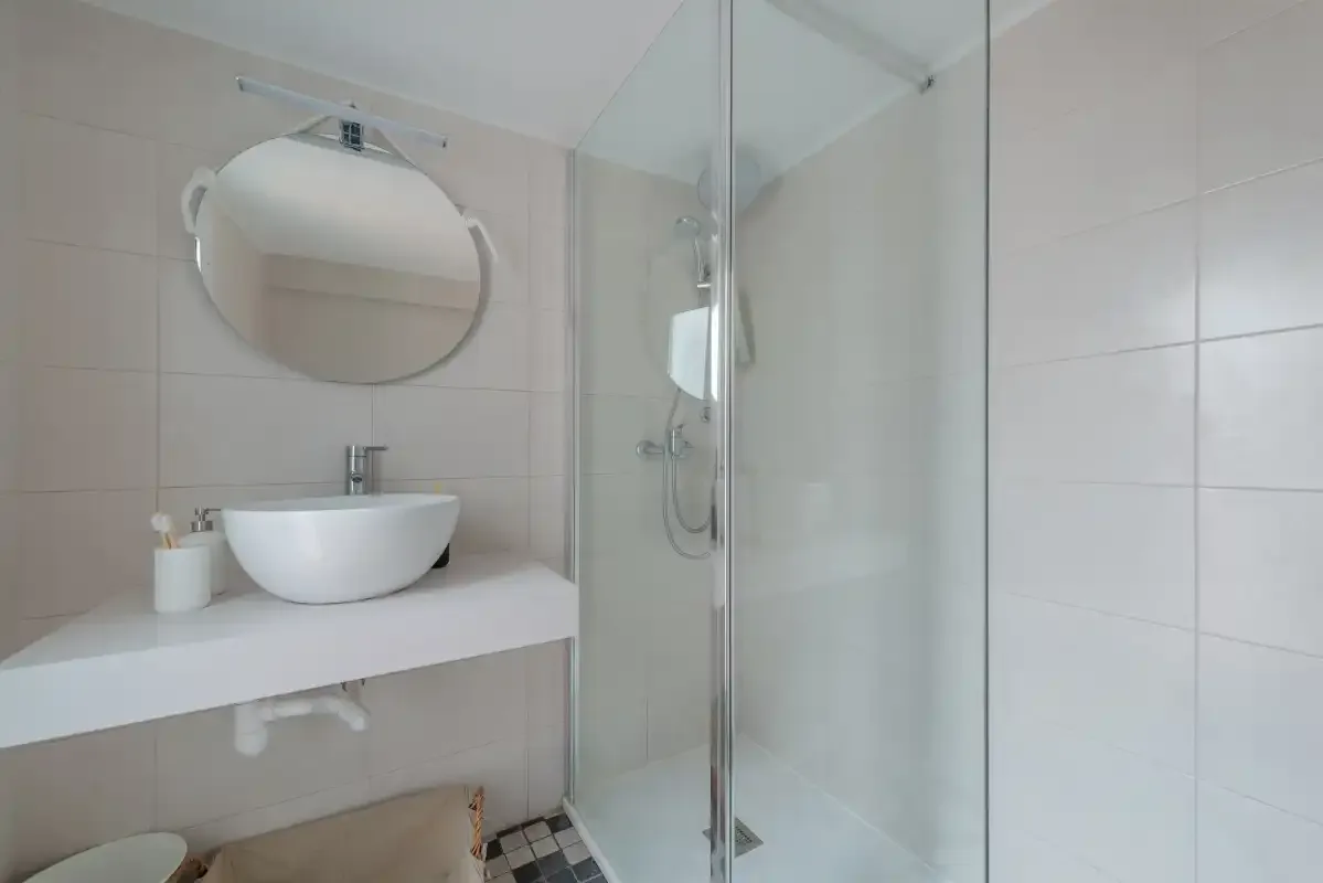 A bright bathroom with a round mirror, vessel sink, and glass shower.