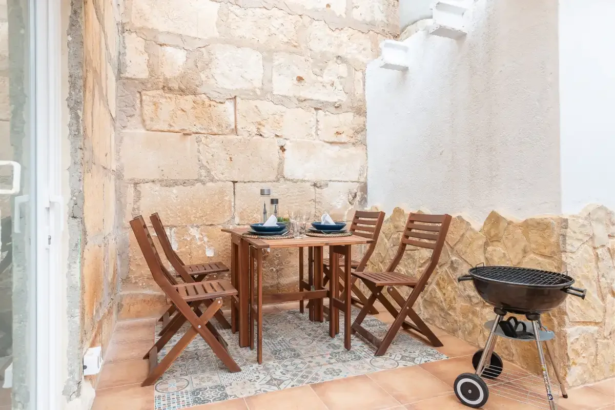 A stone-walled patio with a wooden dining set and a grill.