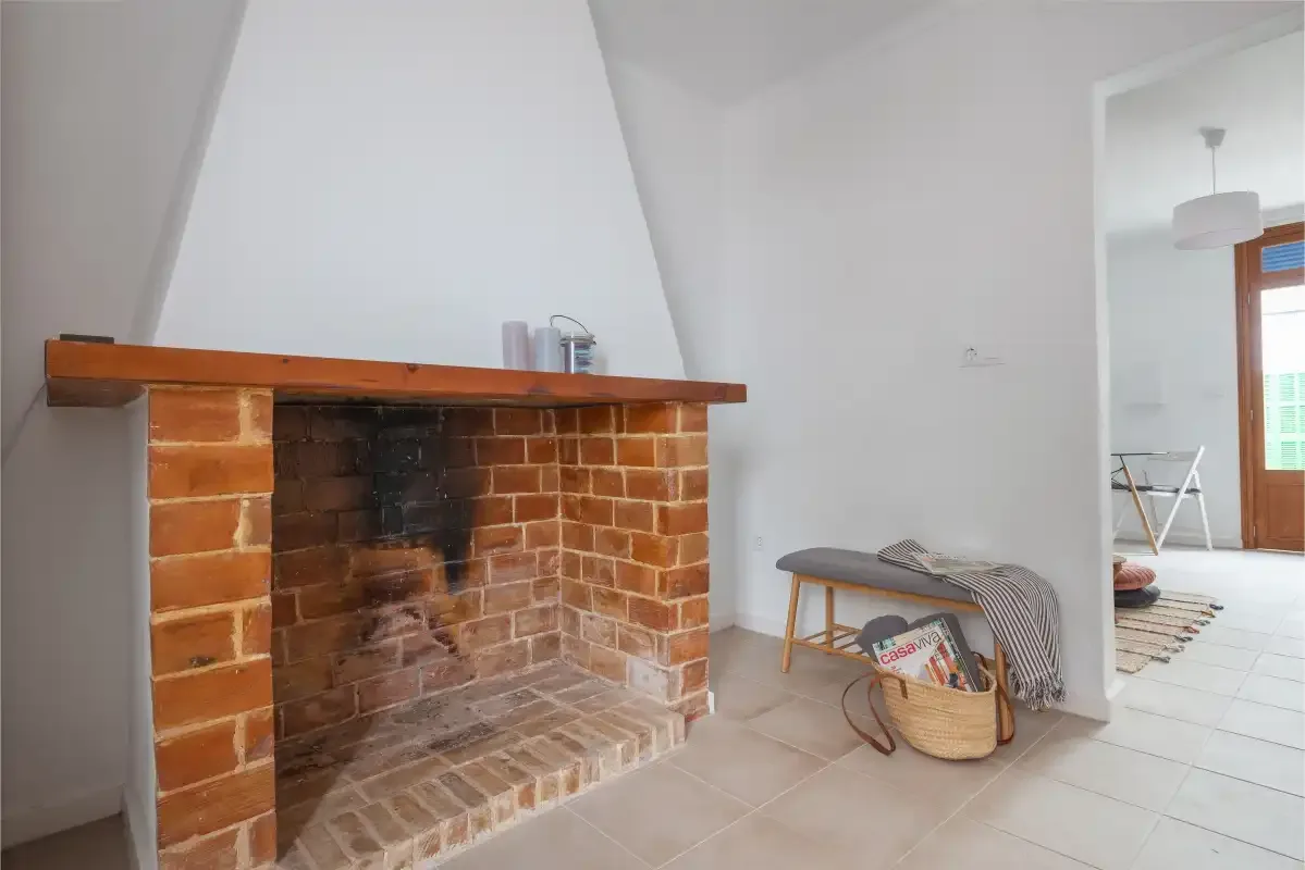 A tiled fireplace stands beside a small seating area in a bright room.