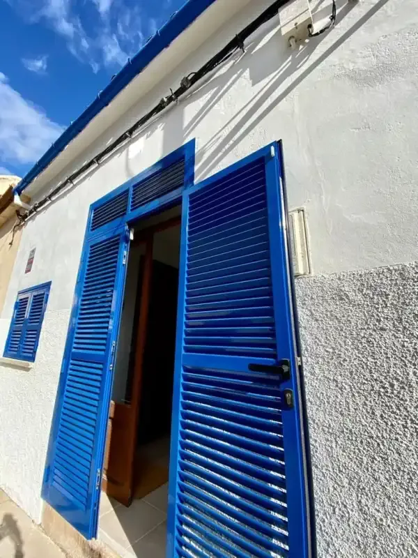 Exterior of a white building with blue shutters open around a doorway.