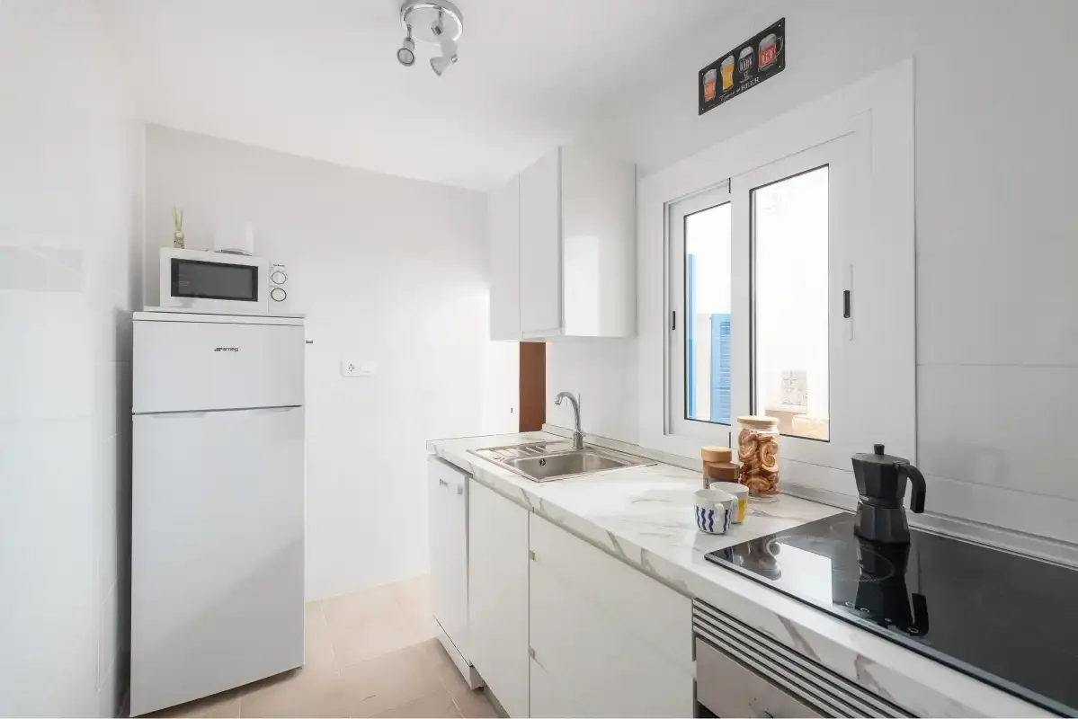 A bright kitchen with white cabinets, a refrigerator, and a cooktop.