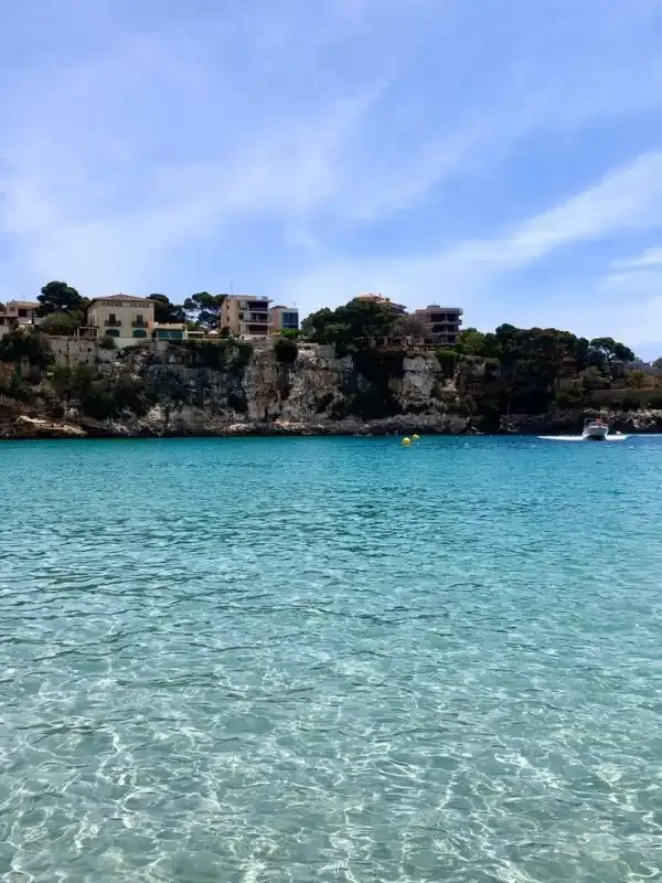 A coastal bay with clear turquoise water and buildings along a rocky shore.