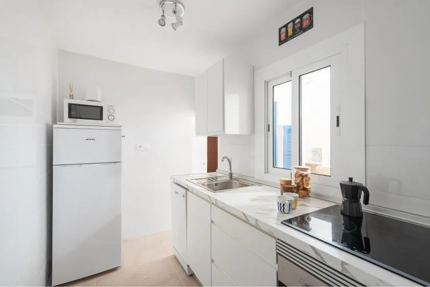 A bright white kitchen with a refrigerator, microwave, and countertop appliances.