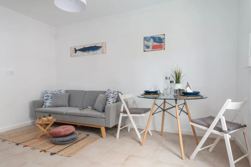 A bright living and dining area with a gray sofa and a round table.