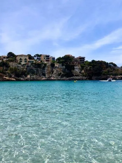 A turquoise bay stretches toward a rocky shoreline with buildings and trees.