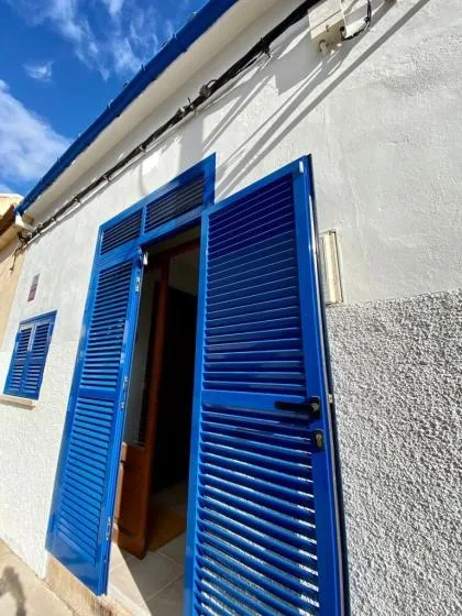 A white exterior wall with an open doorway framed by bright blue louvered shutters.