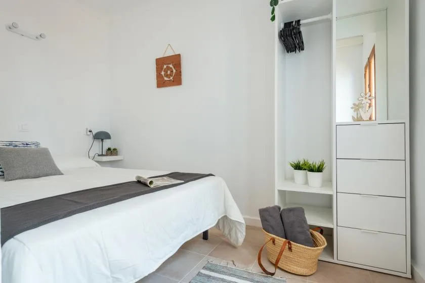 A bright bedroom with a neatly made bed and an open wardrobe.