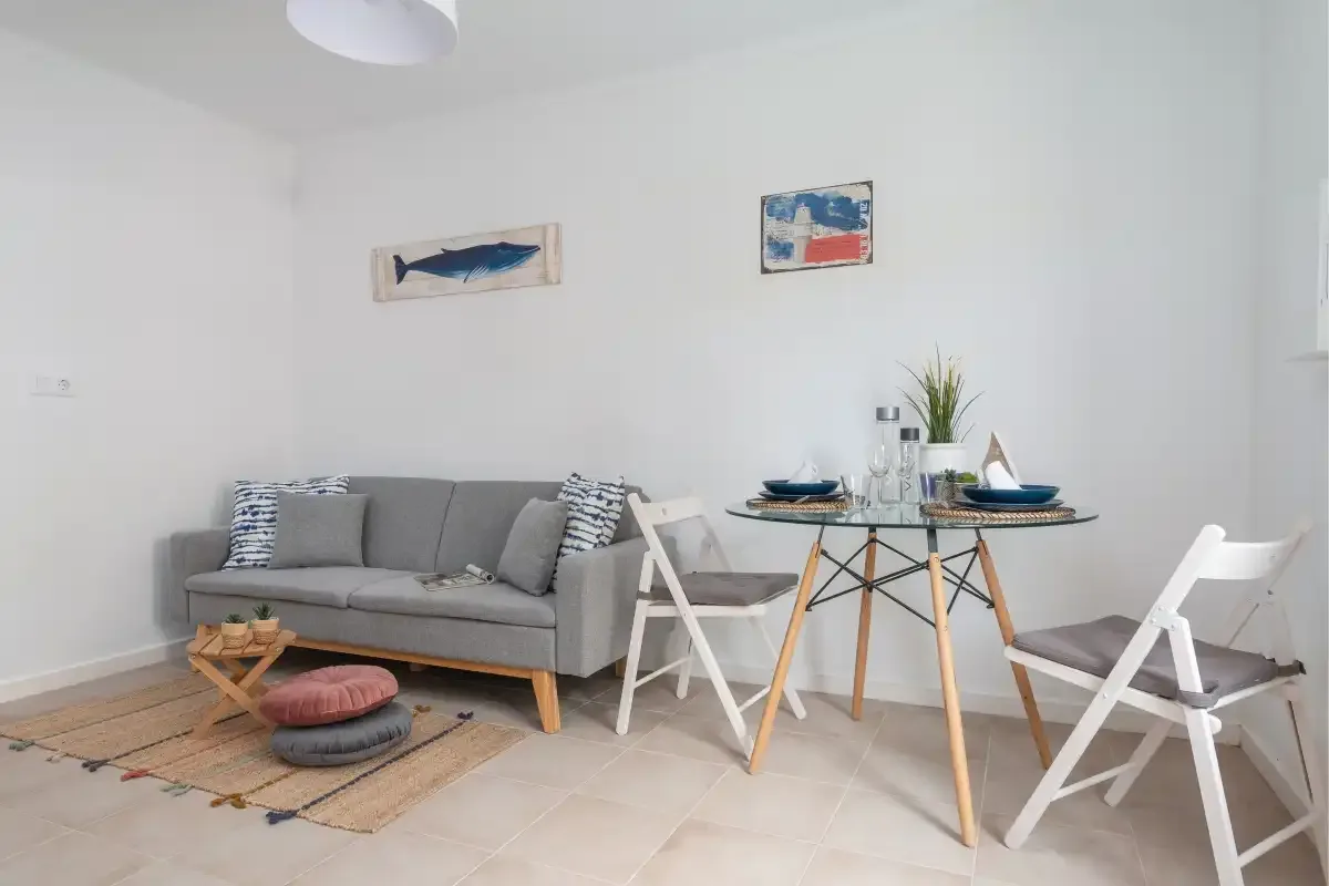 A bright living and dining area with a gray sofa and a round table.