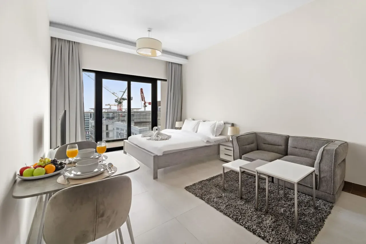A bright bedroom and sitting area with a bed, seating, and large windows.