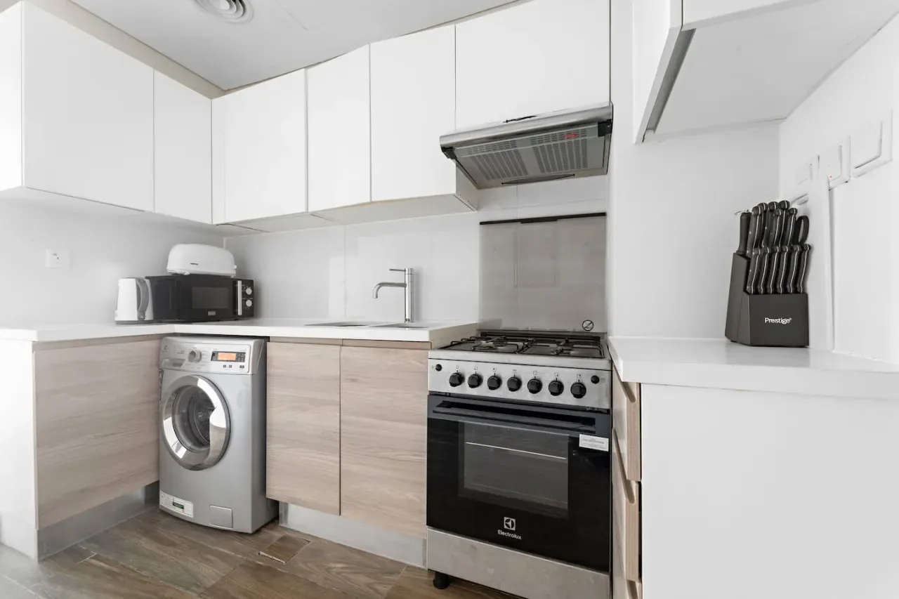 A compact kitchen with white cabinets, a washing machine, and a freestanding stove.