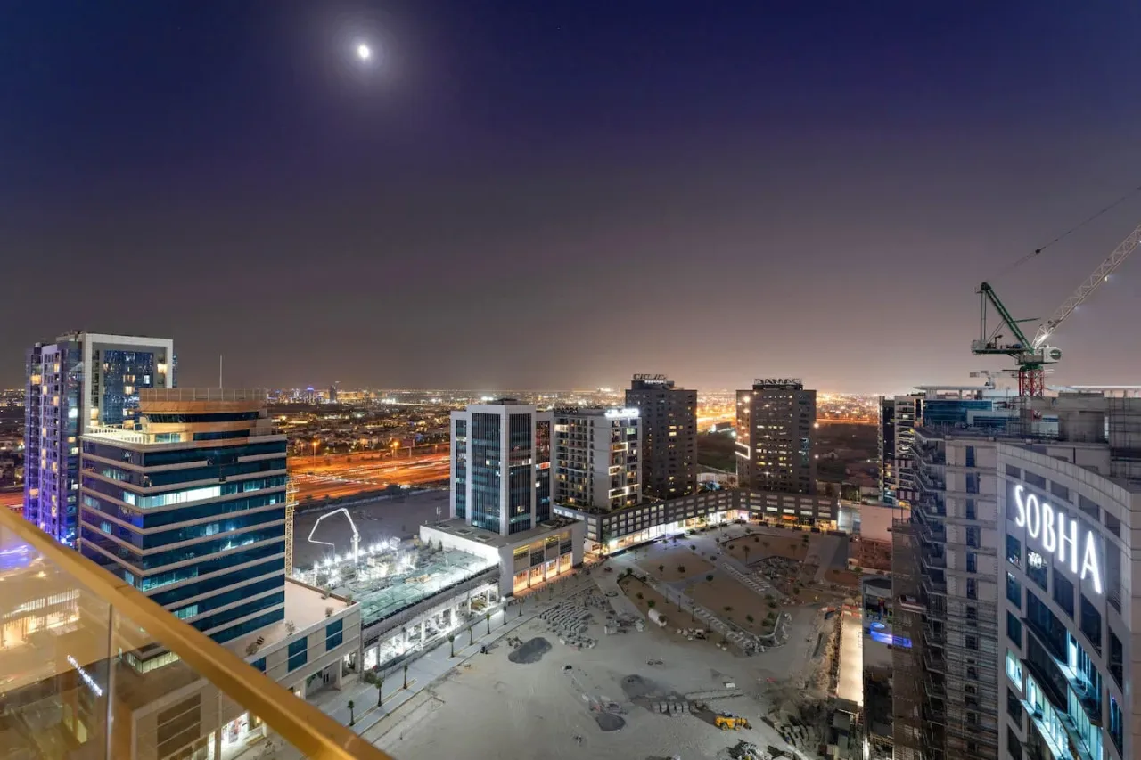 A nighttime city skyline viewed from a balcony, with illuminated buildings and streets.