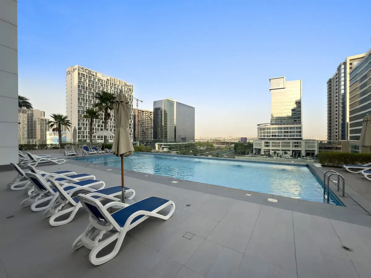 A rooftop swimming pool overlooks modern high-rise buildings, with lounge chairs along the deck.
