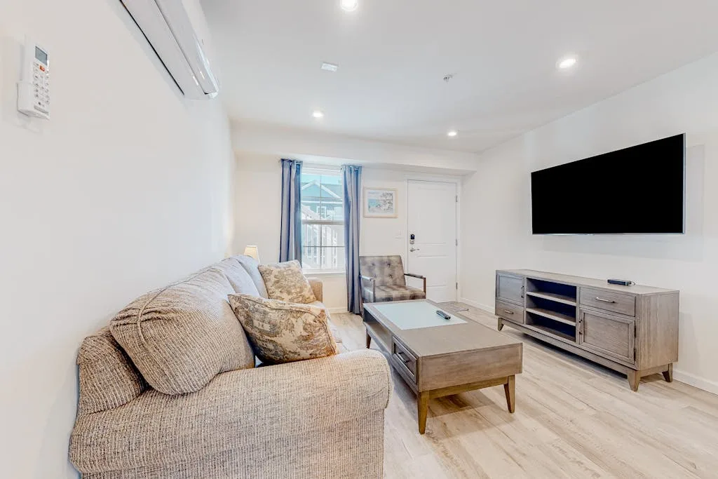 A bright living room with seating, a coffee table, and a wall-mounted television.